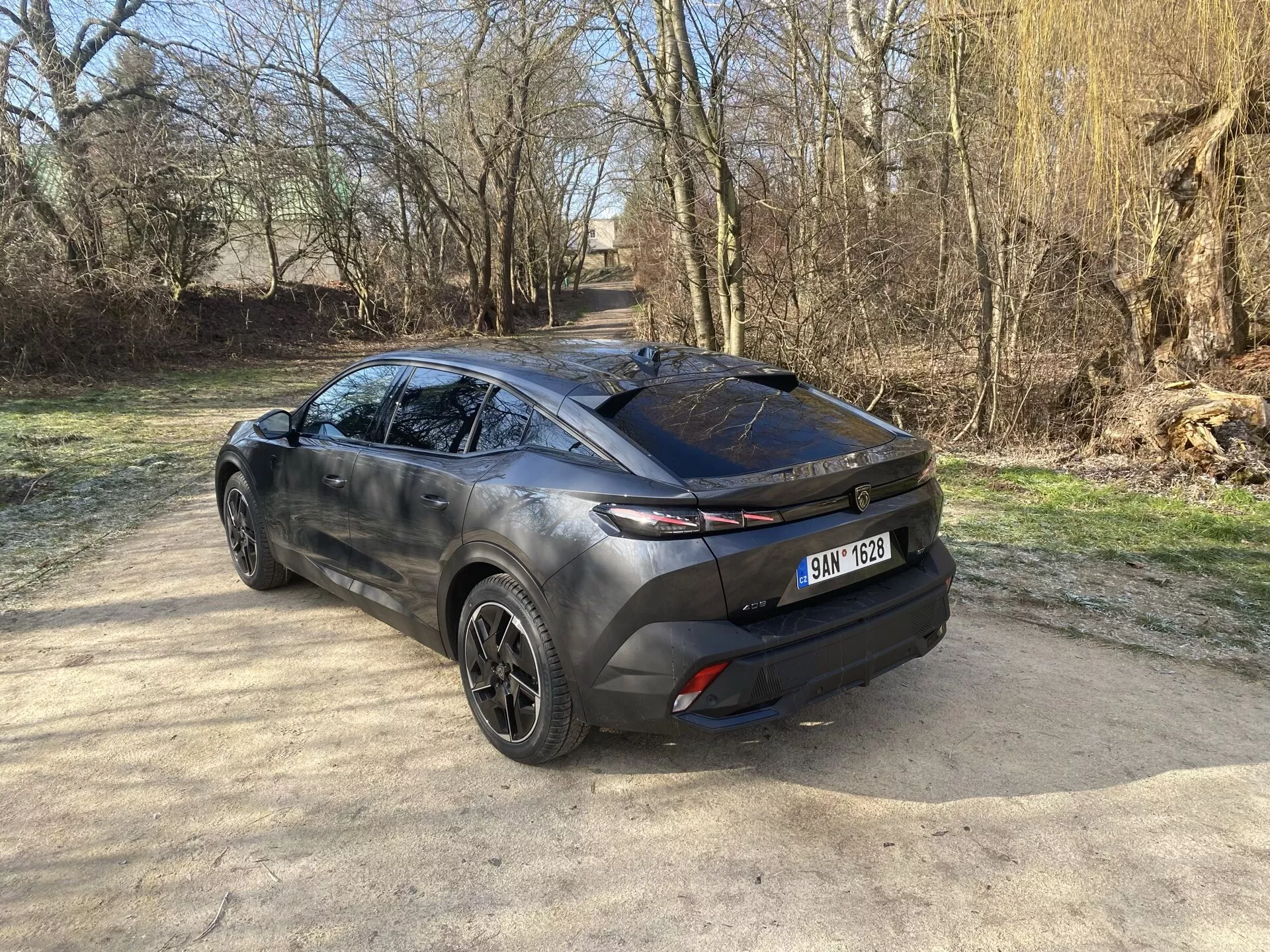 Vue arrière trois-quarts du Peugeot 408 2023 présentant son design moderne de crossover, mettant en avant le hayon, la lunette arrière élégante et les feux arrière horizontaux s'étendant dans le corps latéral, avec un aperçu des jantes en alliage, profil latéral sculpté et peinture bicolore sous la lumière naturelle du soleil
