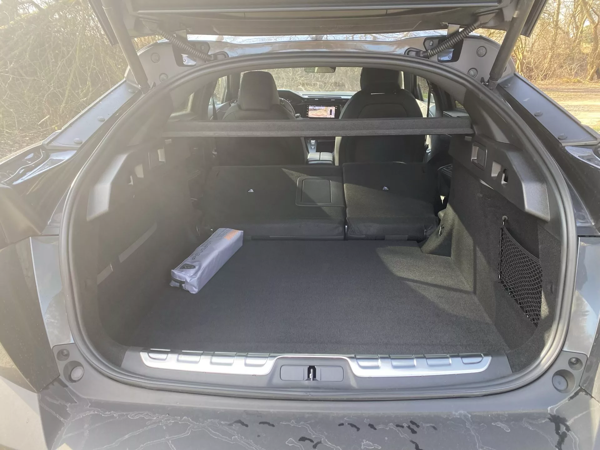 Peugeot 408 première génération 2023 montrant l'espace de chargement intérieur avec les sièges arrière rabattus, vue depuis le hayon arrière en plein jour, démontrant l'espace de chargement, la fonction de sièges arrière rabattables divisés, et sans améliorations technologiques visibles