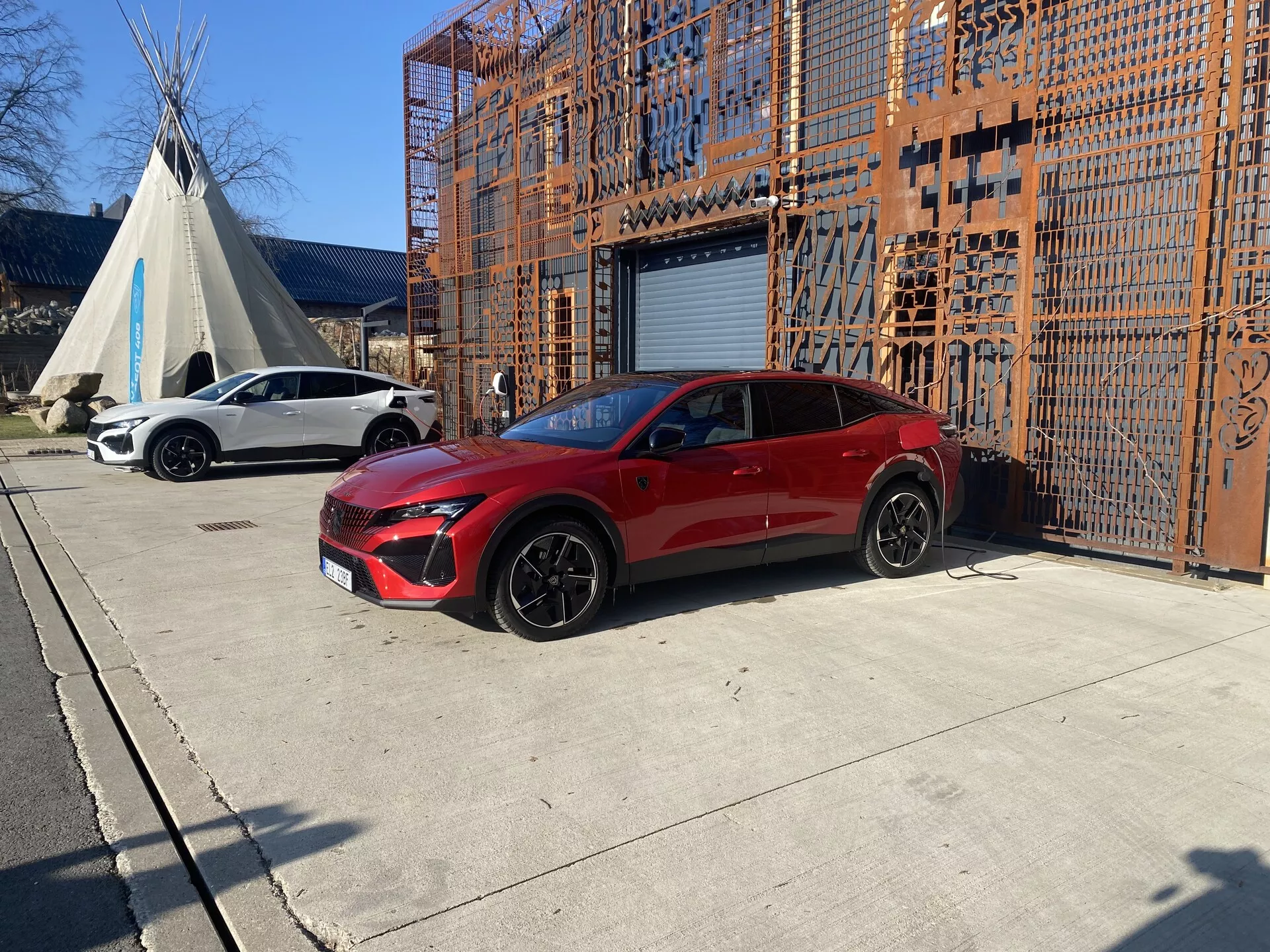 Peugeot 408 2023 en rouge, présentant son design sportif et ses caractéristiques modernes depuis un angle avant de trois quarts, mettant en avant la grille, les phares élancés, les jantes noires sportives et l'élégance de sa carrosserie crossover quatre portes dans un cadre industriel urbain
