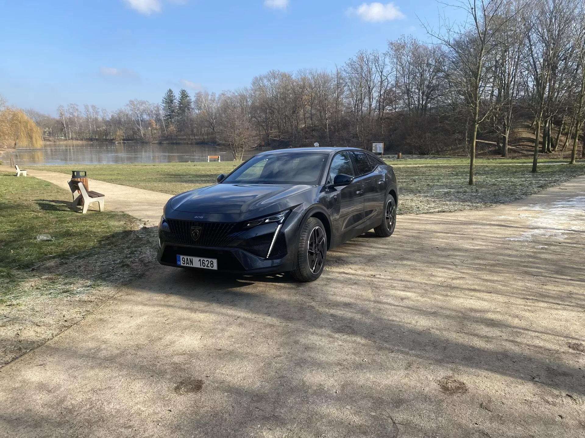 Peugeot 408 de 2023 garée dans un cadre naturel en hiver ou au début du printemps, présentant son design moderne de crossover, phares LED, système de capteurs avant, jantes en alliage et finition premium depuis une vue de trois quarts avant sous la lumière du soleil avec un éclat de lentille.