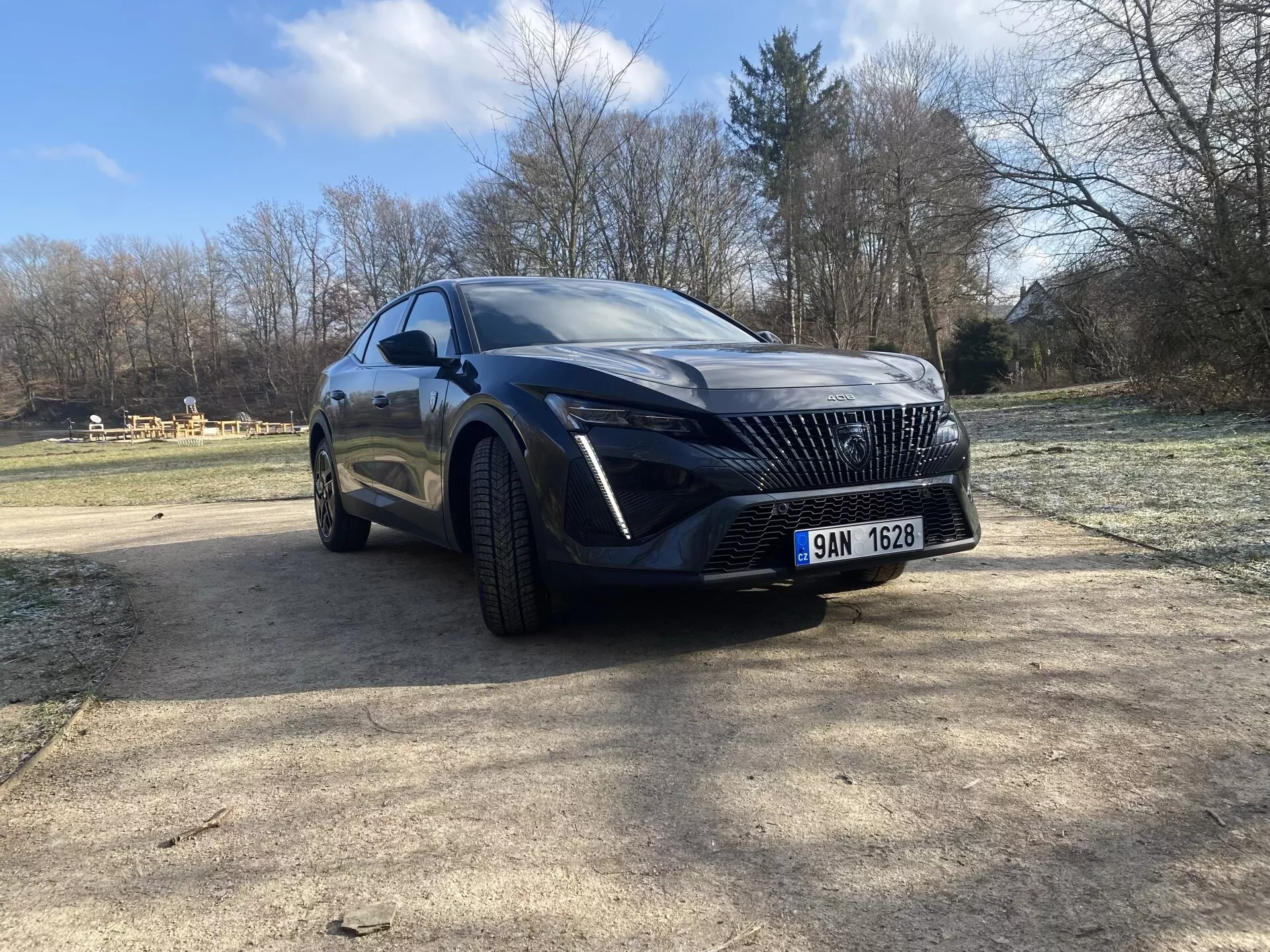 Peugeot 408 2023 capturée sous un angle frontal bas et dynamique mettant en évidence son design sportif agressif, incluant la grille distinctive du SUV de luxe, des phares LED élégants, et une carrosserie aérodynamique sculptée avec une finition brillante, le tout sur un fond naturel bien éclairé.