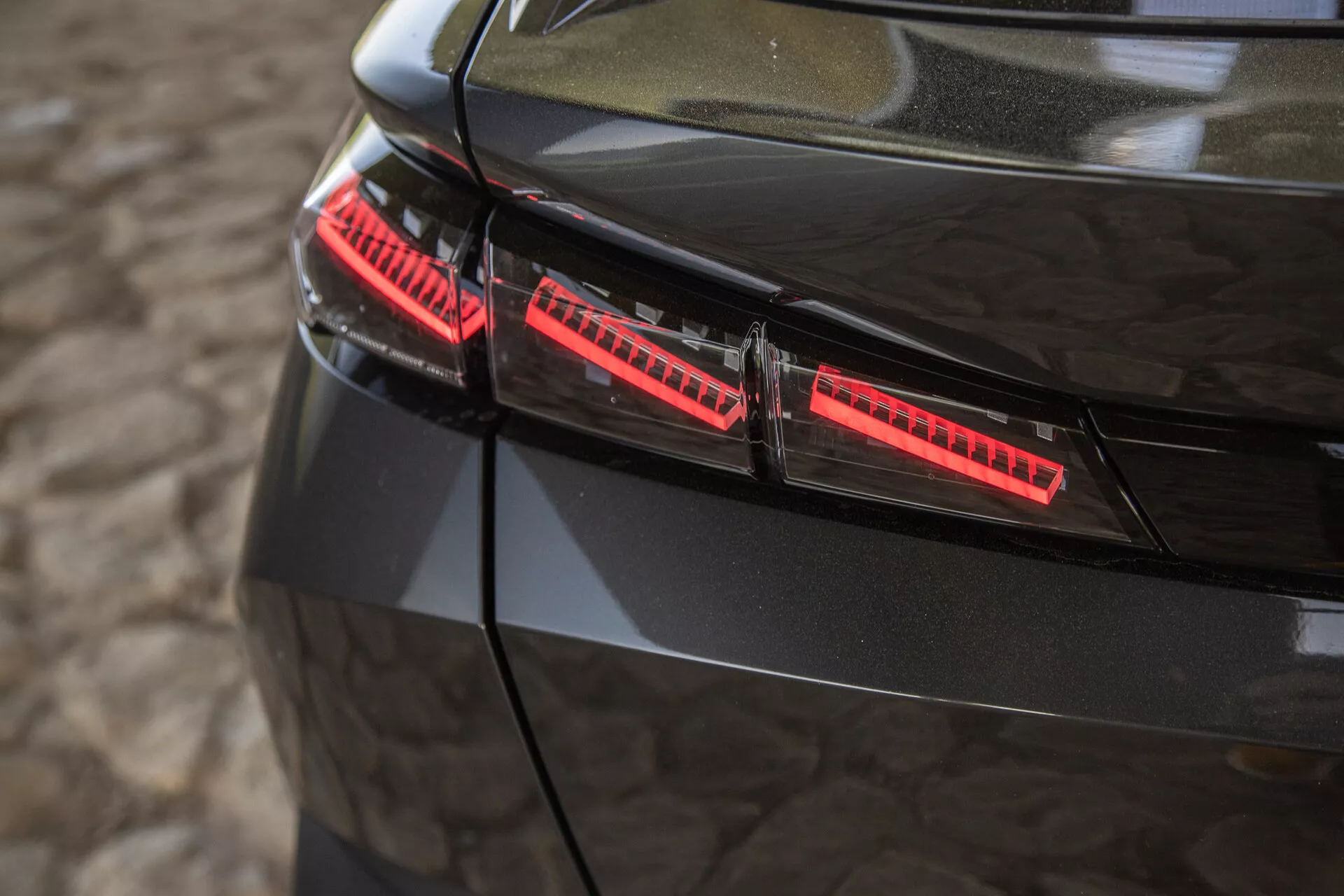 Vue rapprochée des feux arrière noirs brillants de la Peugeot 408 2023, présentant des éléments LED modernes et des accents de design élégants, capturée sous un angle surélevé