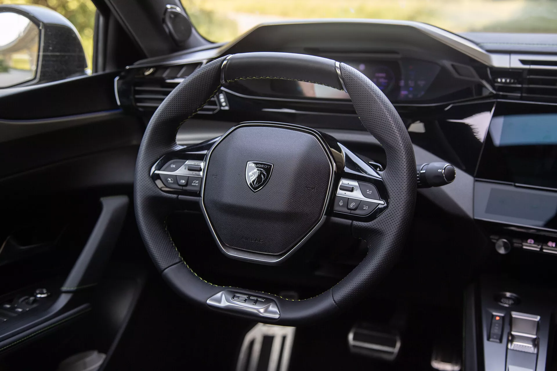 Intérieur du Peugeot 408 2023 présentant un volant moderne multifonction avec logo de marque, tableau de bord numérique en arrière-plan et console centrale partiellement visible avec système d'infodivertissement
