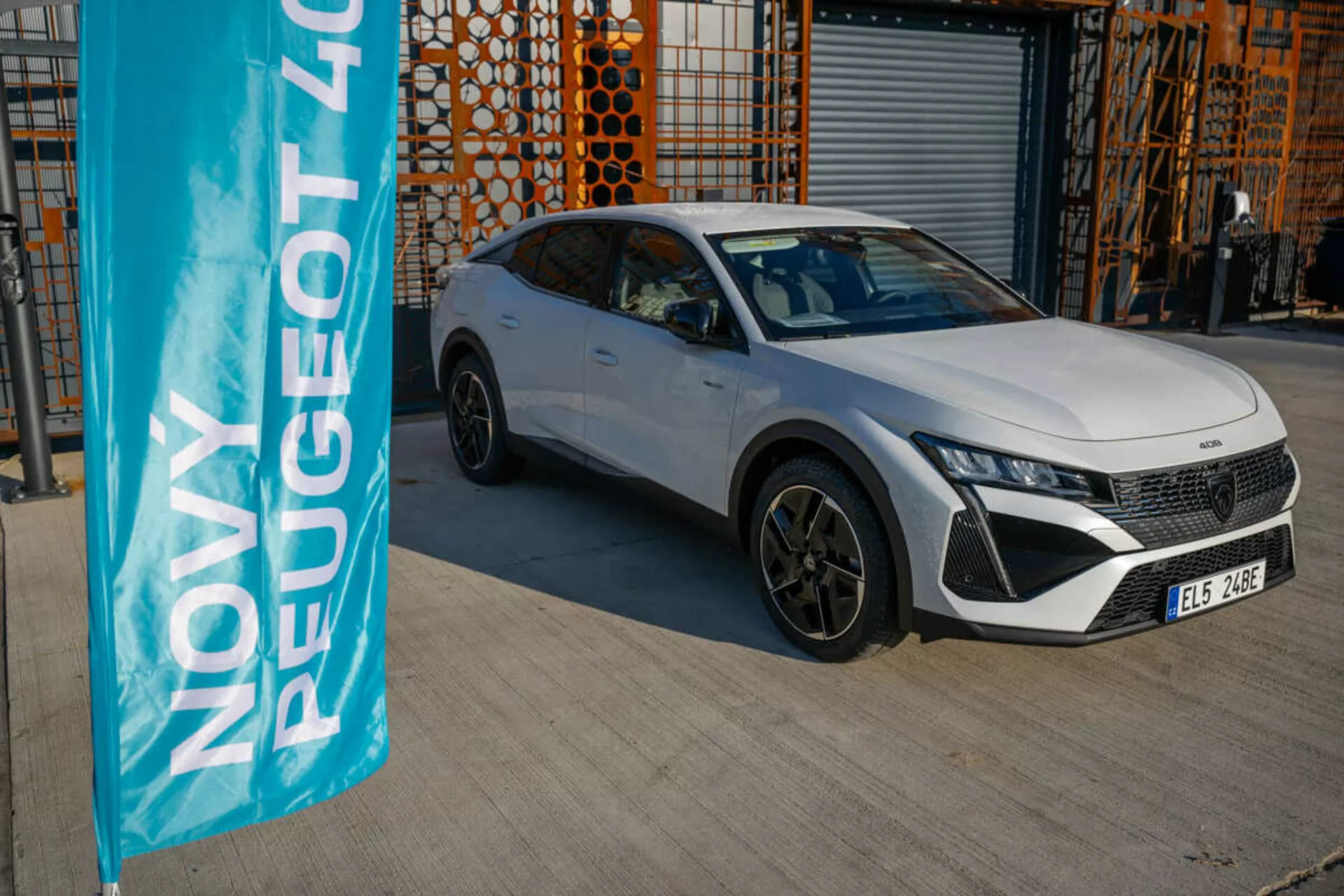 Peugeot 408 blanche 2023 garée en extérieur avec architecture industrielle en arrière-plan, mettant en avant les caractéristiques de design et de technologie du véhicule sous la lumière naturelle du jour