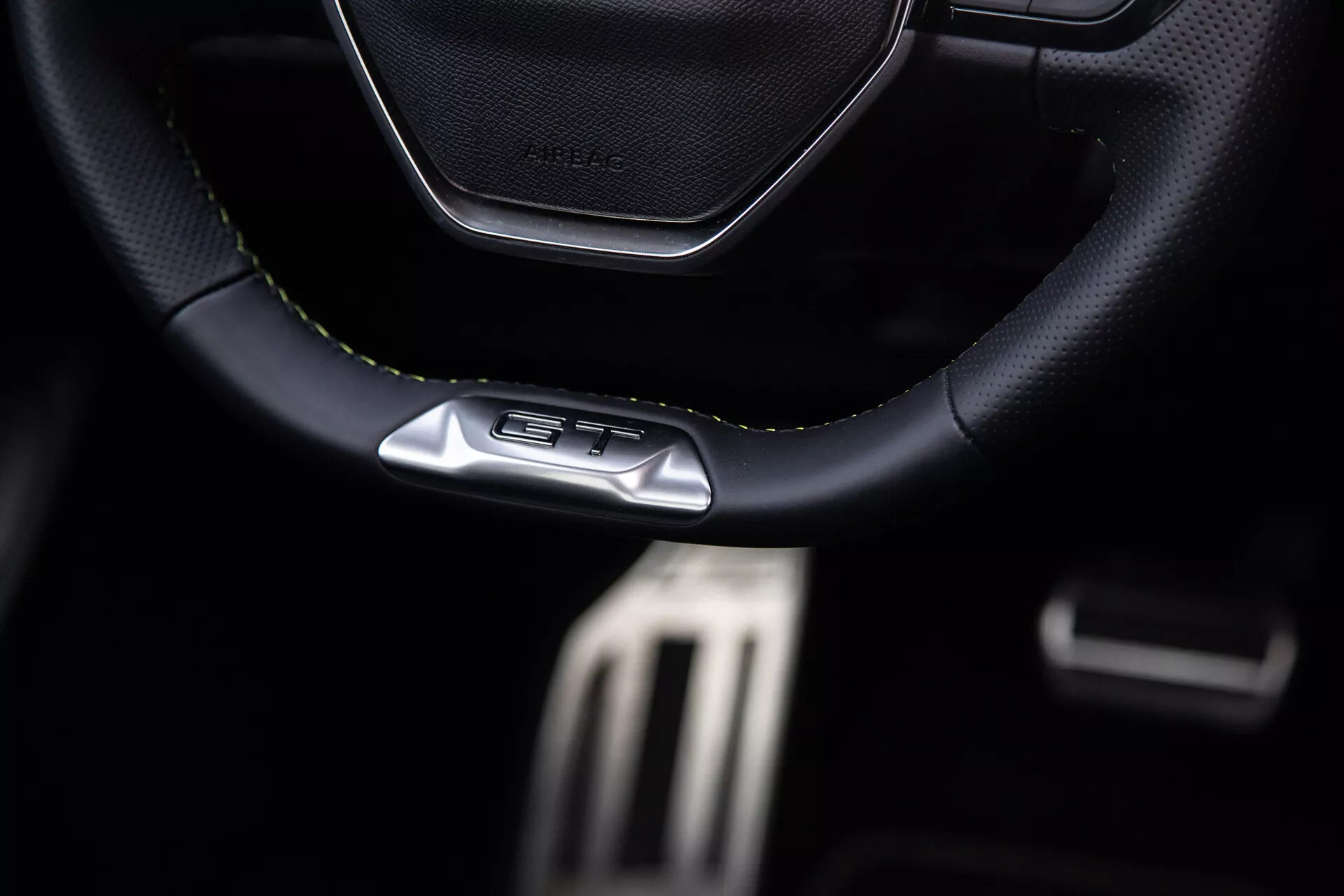 Intérieur du Peugeot 408 2023 mettant en avant le volant sportif cousu en cuir avec l'emblème GT, les pédales métalliques de performance et les caractéristiques premium du cockpit sombre