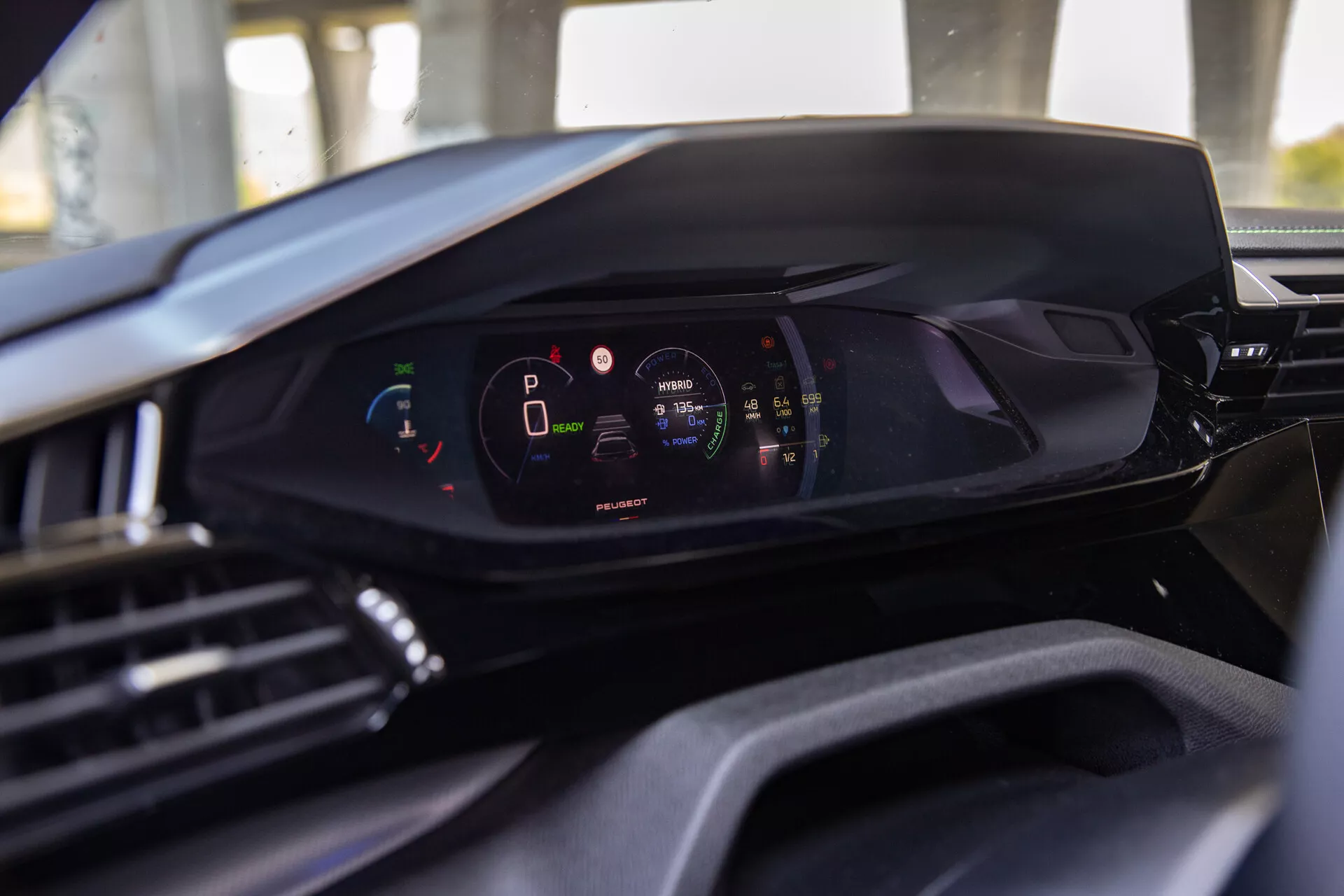 Vue intérieure de la Peugeot 408 2023 mettant en avant le tableau de bord numérique moderne du point de vue du siège conducteur, soulignant le cluster d'instruments numériques avec le véhicule en mode parking et niveau de charge de batterie élevé