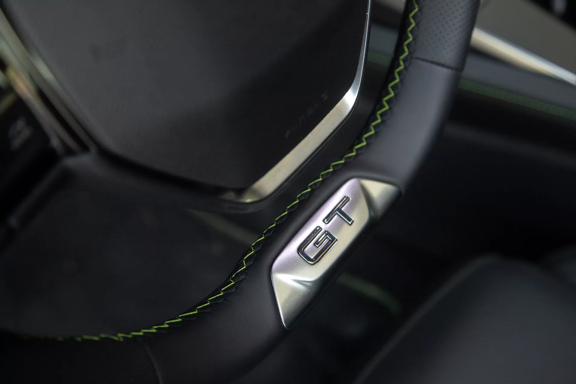 Vue rapprochée de la section du volant et du tableau de bord de la Peugeot 408 2023, mettant en vedette un volant en cuir noir avec coutures vertes et un badge GT, soulignant le luxe et le caractère sportif