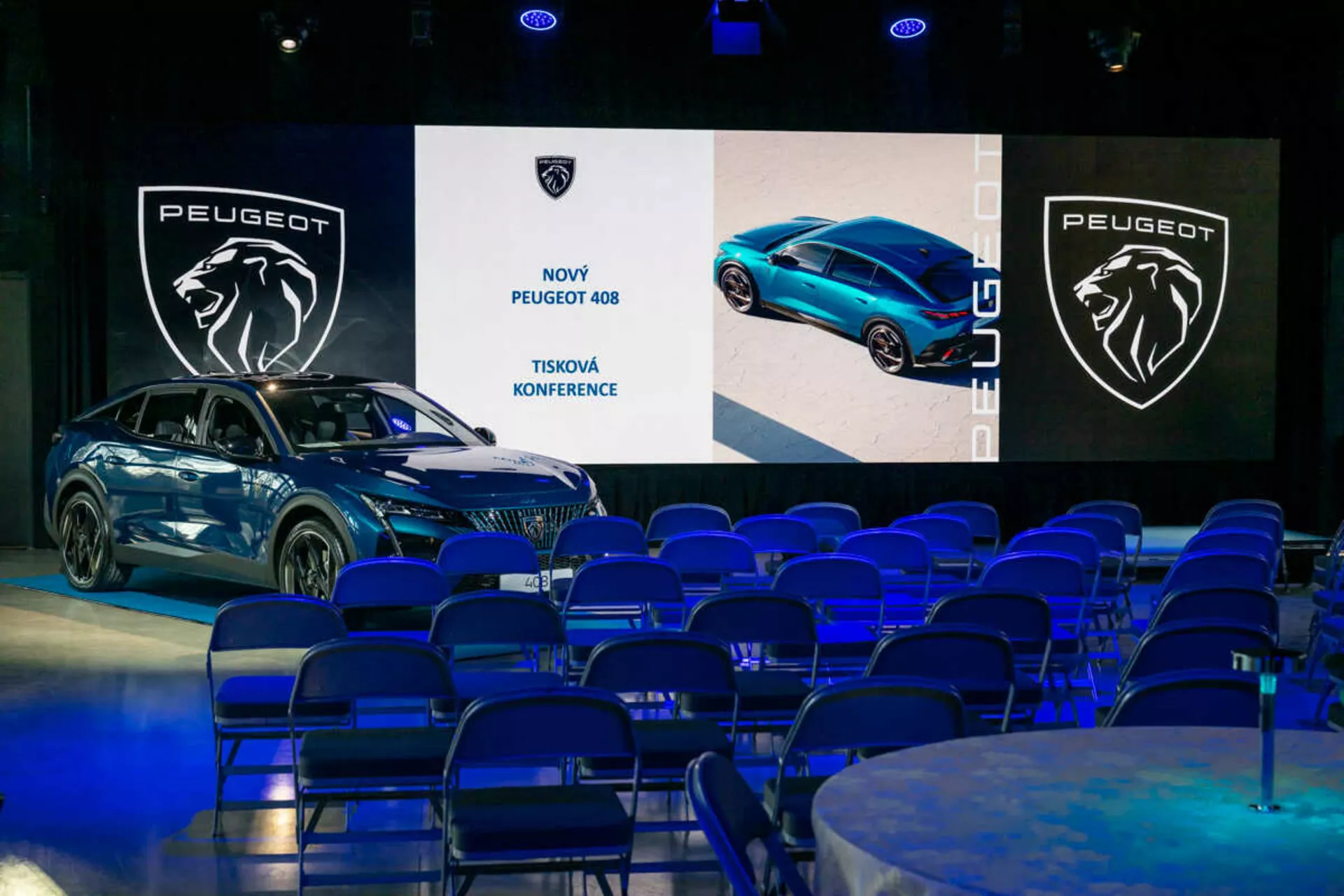 Peugeot 408 présentée lors d'une conférence de presse, vue sous un angle de 45 degrés mettant en avant ses profils avant et latéral, son design élégant et ses phares LED, avec des écrans numériques et un branding en arrière-plan