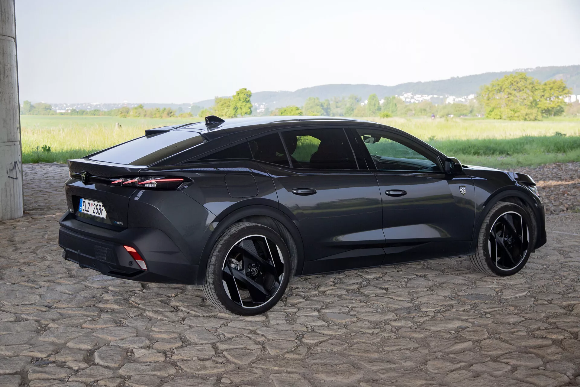 Peugeot 408 de 2023 capturée depuis un angle arrière trois quarts mettant en avant son design sportif de hayon, spoiler arrière intégré avec feux arrière sur toute la longueur, jantes en alliage noir et caractéristiques contemporaines comme des poignées de porte affleurantes et des rétroviseurs latéraux avec clignotants, à la lumière naturelle du jour
