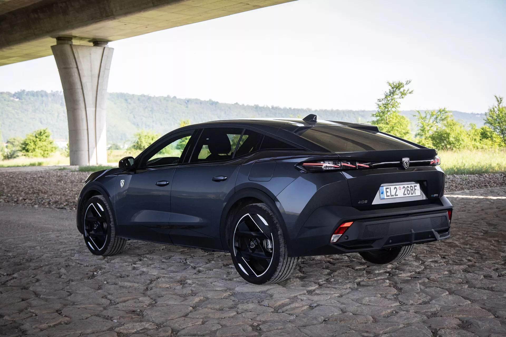 Vue arrière trois quarts d'une Peugeot 408 hatchback 2023 sous un pont sur pavés avec jantes sportives et technologie d'éclairage avancée