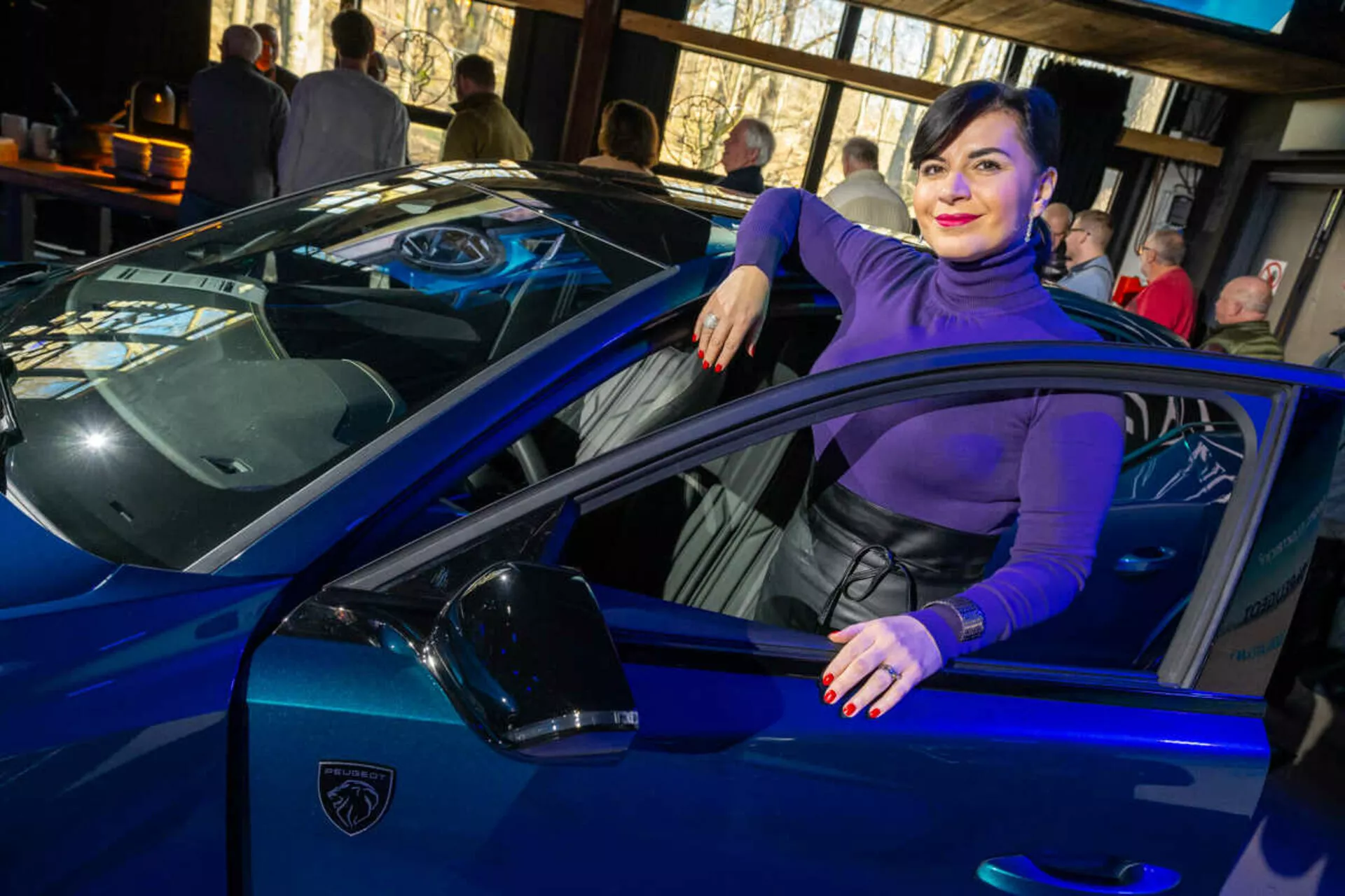 Voiture de sport bleu vibrant, possiblement une Lamborghini, capturée depuis un angle de trois quarts mettant en évidence ses lignes épurées, ses phares LED aiguisés et son emblème iconique en forme de bouclier, avec une personne interagissant décontractée avec le véhicule suggérant luxe et style.