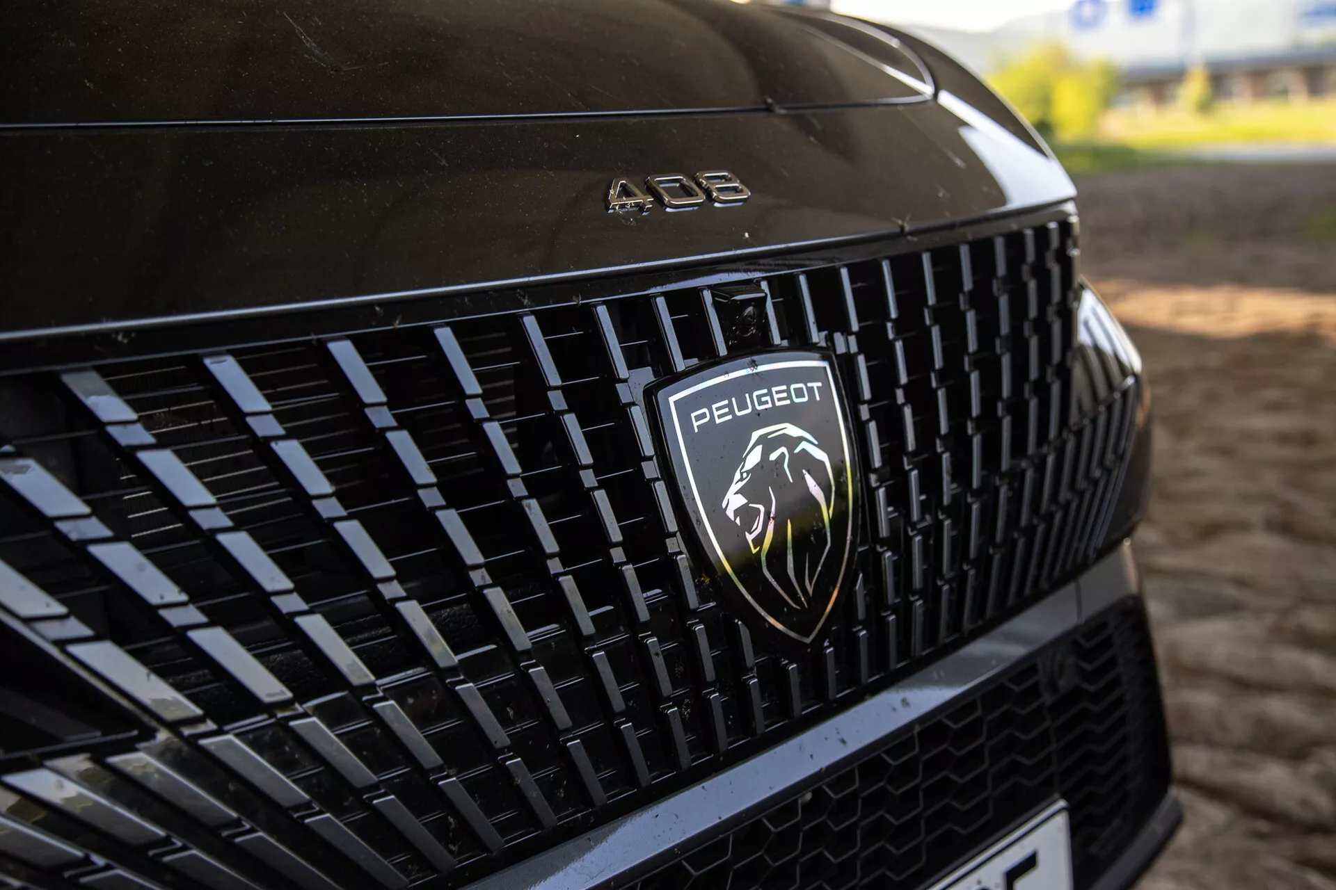 Vue détaillée de la grille avant du Peugeot 408 2023 montrant le motif complexe et le logo du lion argenté, sous un éclairage naturel