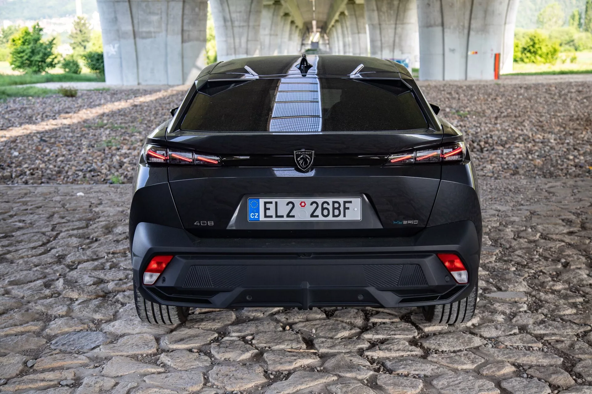 Vue arrière directe de la variante électrique de la Peugeot 208 (e-208) montrant la plaque d'immatriculation, le pare-brise arrière avec essuie-glace, les feux arrière intégrés, le logo Peugeot, le diffuseur arrière sportif et l'indicateur de port de chargement électrique