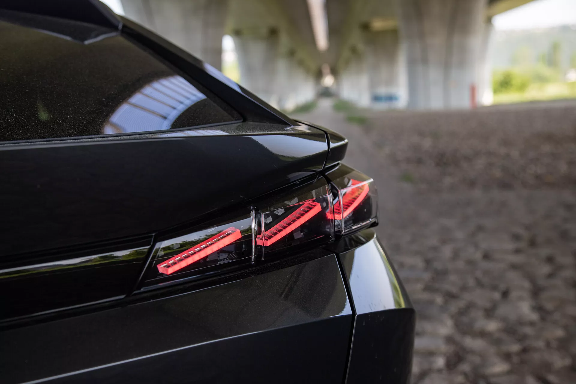Gros plan sur l'arrière de la Peugeot 408 de 2023 avec feu arrière LED, design élégant du coffre avec spoiler intégré et finition noire brillante sous une ombre structurée