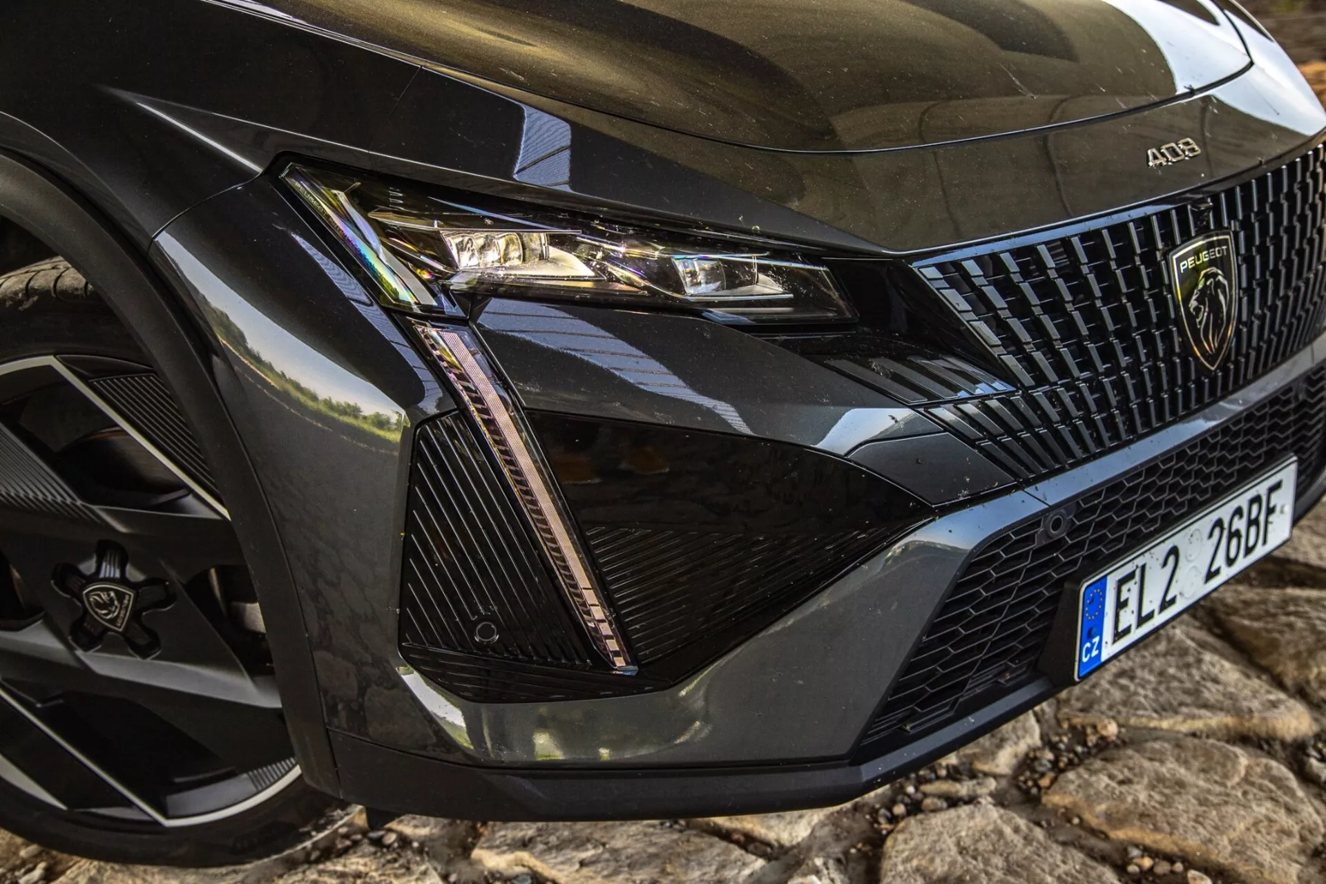 Gros plan sur le coin avant gauche du Peugeot 408 2023 montrant l'ensemble phare détaillé, la section de la grille, le capot et la roue avec technologie LED moderne et éléments de design de luxe.