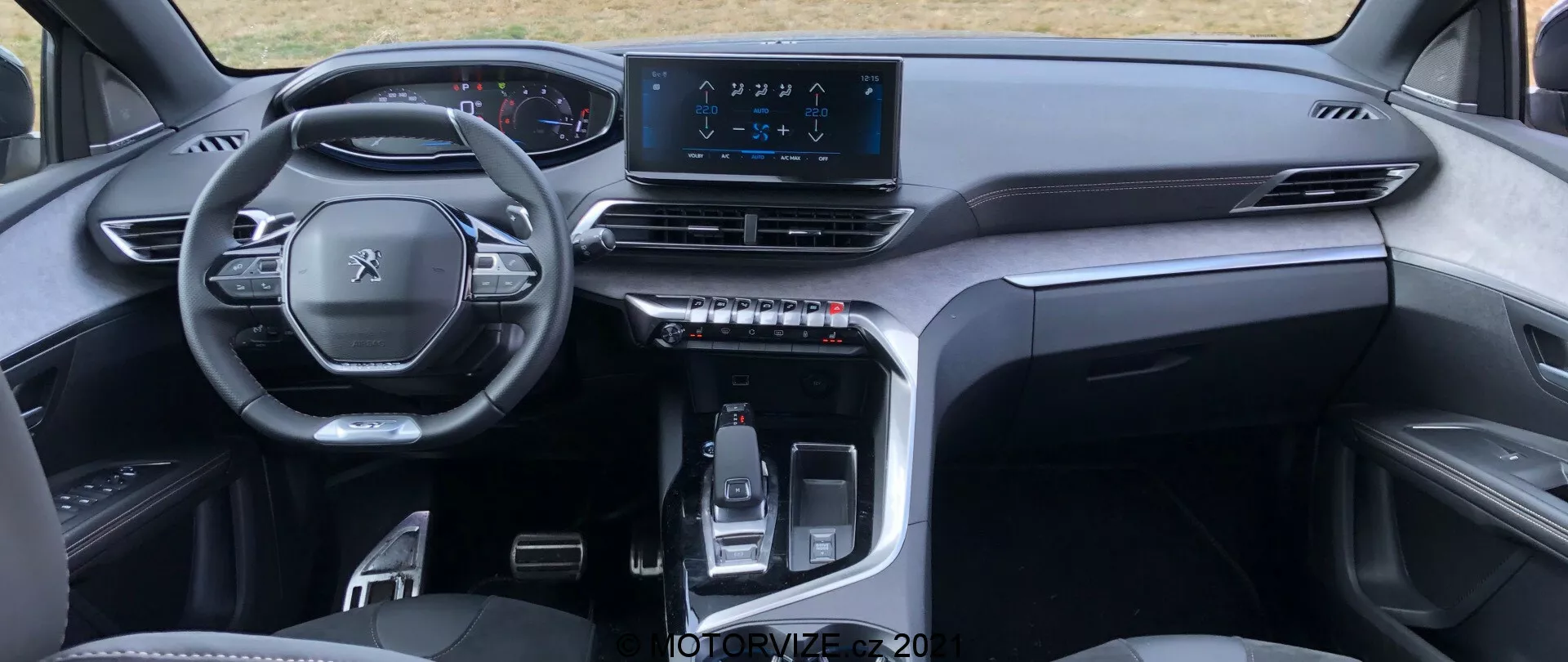 Vue intérieure de la Peugeot 5008 2021 depuis la perspective de la banquette arrière, mettant en évidence un volant multifonction, un tableau de bord numérique, un tableau de bord symétrique avec des bouches d'aération, un écran tactile central de divertissement et une console centrale élégante avec un levier de vitesses contrôlé électroniquement et des boutons tactiles. Le design élégant et minimaliste utilise des matériaux de haute qualité, suggérant un véhicule moderne et premium.