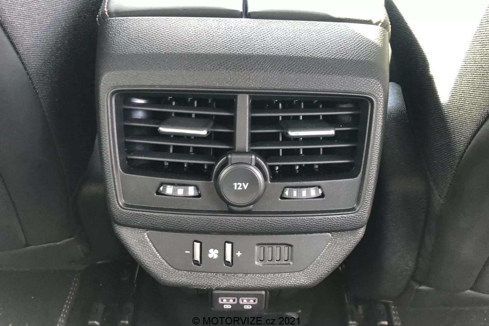 Vue rapprochée des caractéristiques pour les passagers arrière sur le dos de la console centrale dans la Peugeot 5008 2021. L'image montre des bouches d'aération doubles, une prise de courant 12V, des contrôles de chauffage des sièges, des ports USB et un bouton vierge, capturée depuis la perspective d'un occupant des sièges arrière.