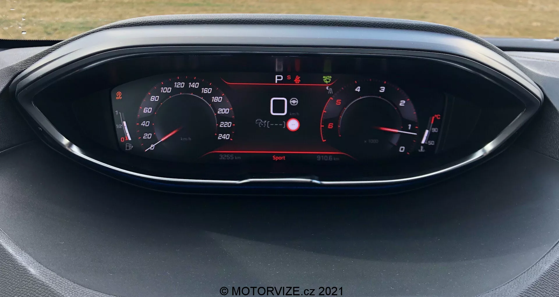 Vue rapprochée du tableau de bord d'un Peugeot 5008 de 2021, avec un affichage numérique et des jauges de style analogique. L'affichage montre le compteur de vitesse, le compte-tours, la sélection des vitesses et divers indicateurs de véhicule comme les avertissements de sécurité et le mode de conduite. La voiture est à l'arrêt avec le mode de conduite 'Sport' activé.