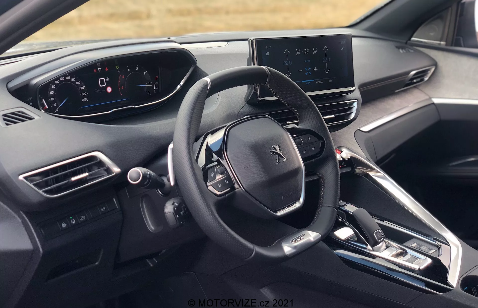 Vue intérieure de la Peugeot 5008 2021 depuis la perspective du conducteur, montrant le volant avec le logo Peugeot, plusieurs boutons de commande, tableau de bord entièrement numérique, écran central d'infodivertissement avec carte de navigation, tableau de bord élégant avec peu de boutons physiques, console centrale avec boutons pour le contrôle de la climatisation et les réglages du véhicule, levier de changement de vitesse électronique, bouches d'aération, bouton de démarrage/arrêt du moteur, matériaux de haute gamme et vue partielle de l'appuie-tête du siège conducteur.