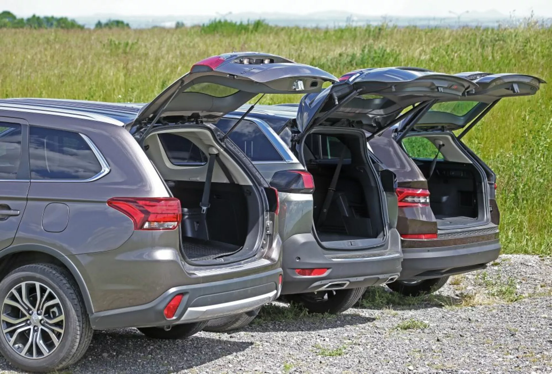 Vue arrière de trois SUV Peugeot 5008 de 2013 garés côte à côte montrant leurs hayons automatiques, antennes satellites et roues en alliage contre un arrière-plan rural à la lumière naturelle du jour