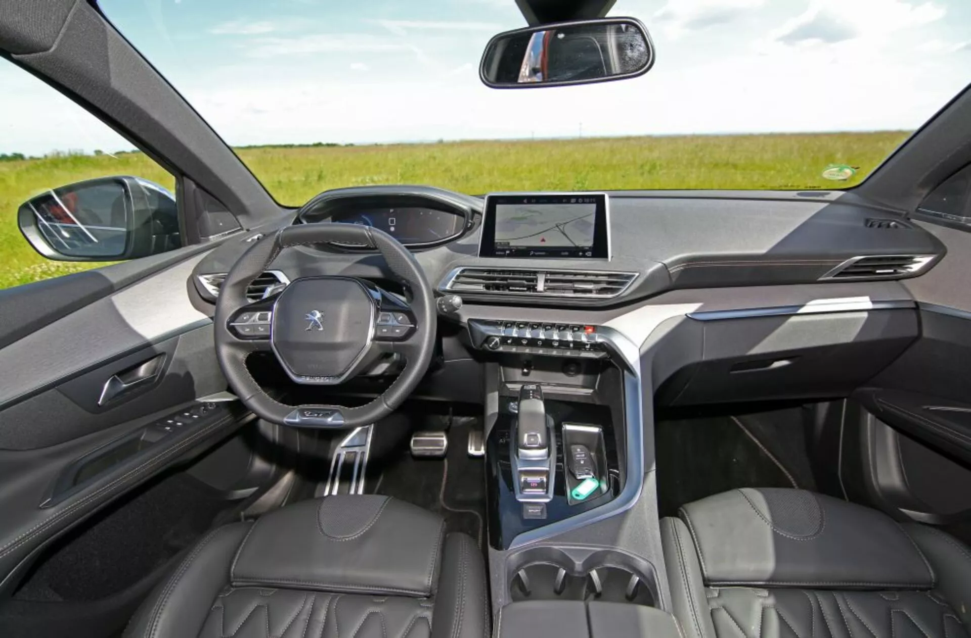 Vue intérieure d'une Peugeot 5008 de 2013 depuis les sièges arrières mettant en avant le tableau de bord, avec des sièges avant en cuir de haute qualité, tableau de bord numérique, volant Peugeot avec commandes intégrées, système d'infodivertissement tactile central et panneau de commande central moderne, sous un éclairage naturel ambiant