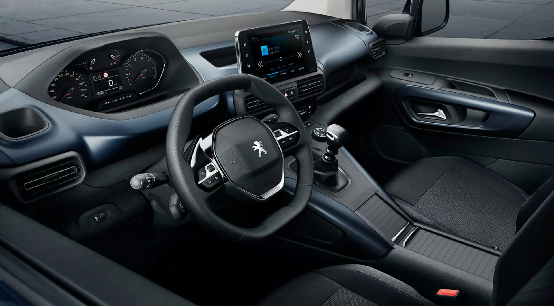 Vue surélevée de l'intérieur du Peugeot Rifter 2018 mettant en vedette un système d'infodivertissement tactile, un tableau de bord numérique, et un volant à trois branches avec commandes intégrées, soulignant l'excellence technologique et de conception