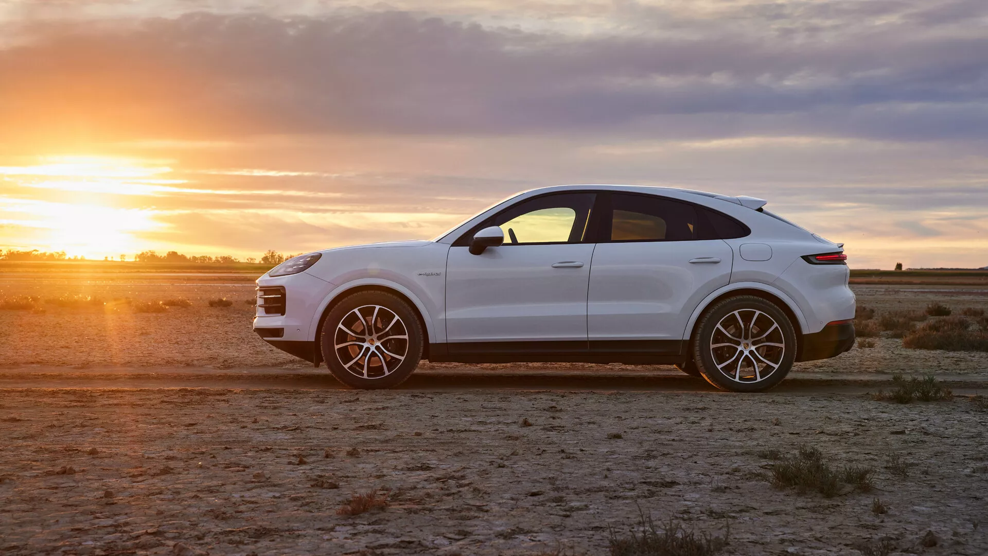 SUV crossover de luxe Porsche Cayenne 2023 en blanc brillant sur terrain aride à l'heure dorée, présentant une vue de profil, des roues en alliage sportives et des caractéristiques de conception élégantes