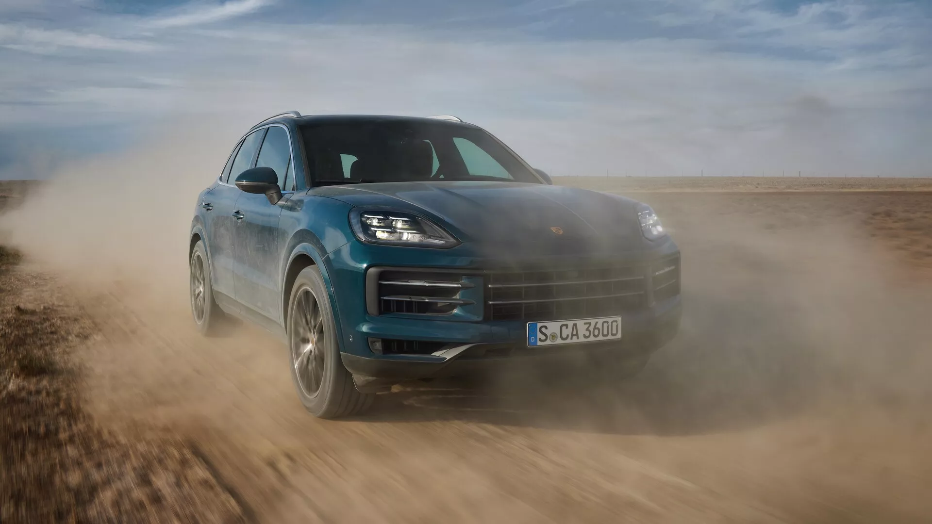 Porsche Cayenne 2023 (facelift 9YA) en mouvement dynamique, présentant son design élégant et ses capacités tout-terrain, capturée sous un angle avant bas de trois quarts soulignant la posture sportive, phares LED avancés et caractéristiques aérodynamiques sur une surface non pavée.
