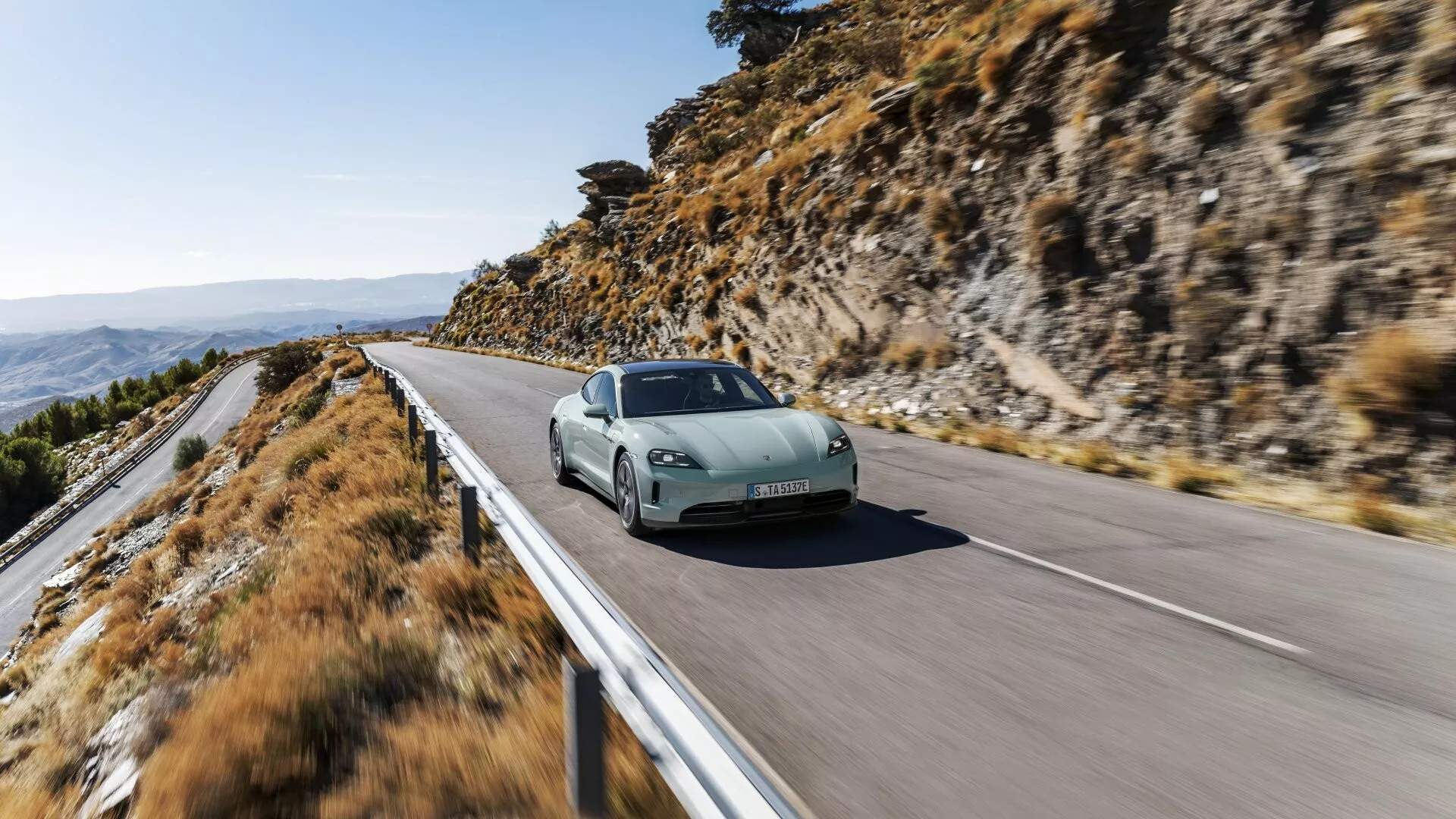 Porsche Taycan 2024 (Y1A Facelift) en mouvement sur une route montagneuse montrant un design aérodynamique, des phares LED et des jantes sportives