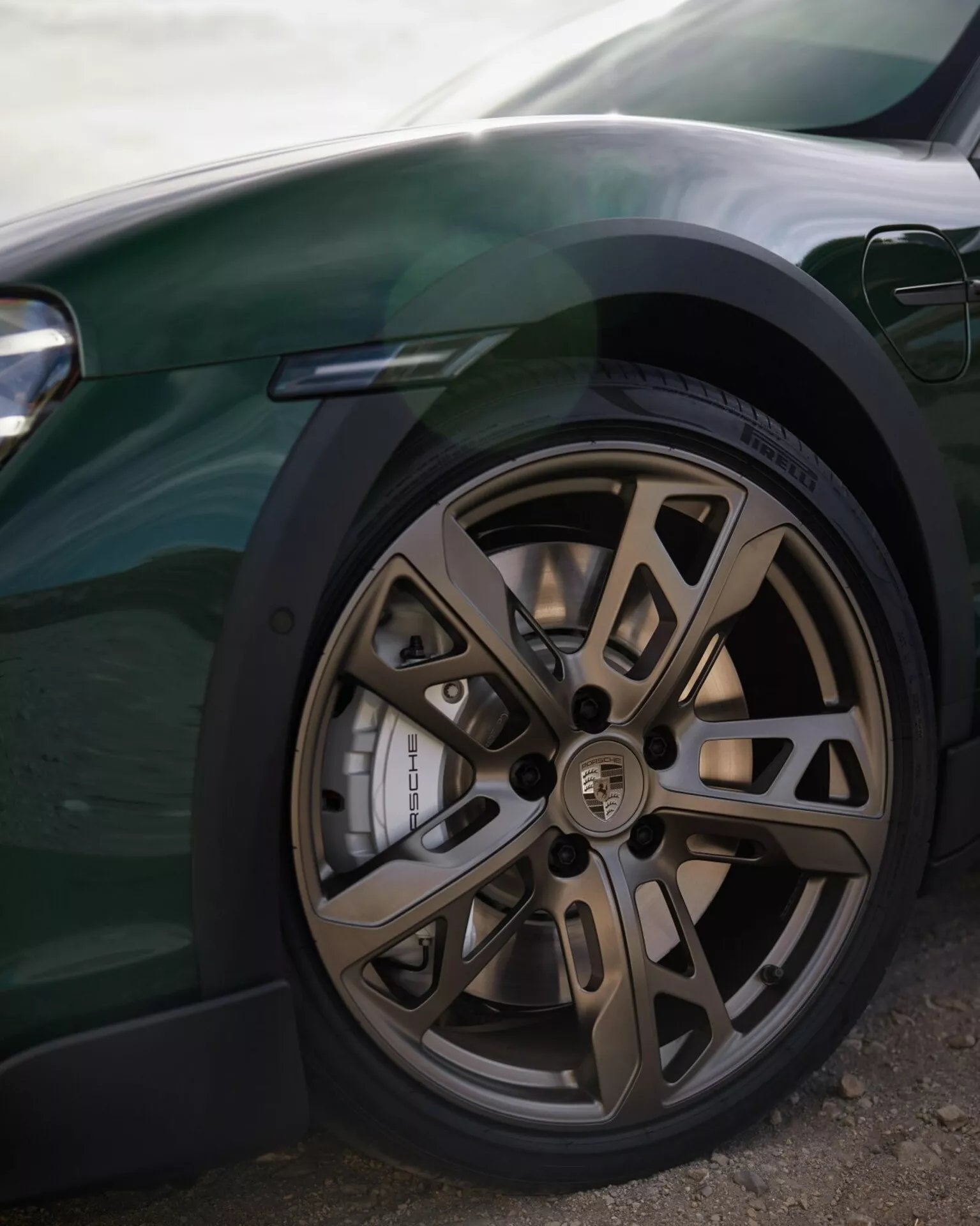 Vue rapprochée de la roue avant d'une voiture de luxe haute performance présentant un design en alliage bronze à multiples branches, un pneu à faible profil, un disque de frein perforé avancé et une étrier de taille importante contre une carrosserie sombre élégante, avec un aperçu du système d'éclairage moderne.