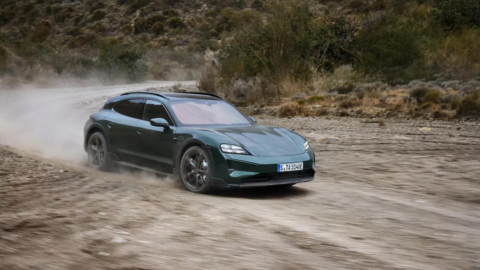 Vue dynamique de la Porsche Taycan 2024 (Y1A facelift) en mouvement sur une route non pavée, mettant en évidence ses phares LED, design aérodynamique, roues en alliage et traînée de poussière indiquant une grande vitesse et des capacités à traction intégrale.
