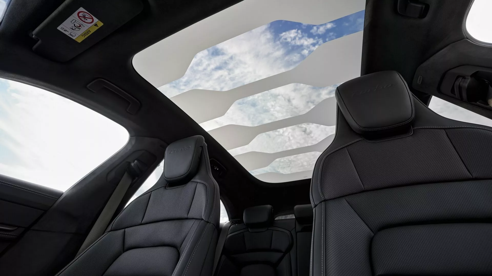 Vue intérieure d'une Porsche Taycan 2024 avec toit panoramique et sièges en cuir noir haut de gamme, mettant en évidence les caractéristiques de luxe et les technologies de sécurité