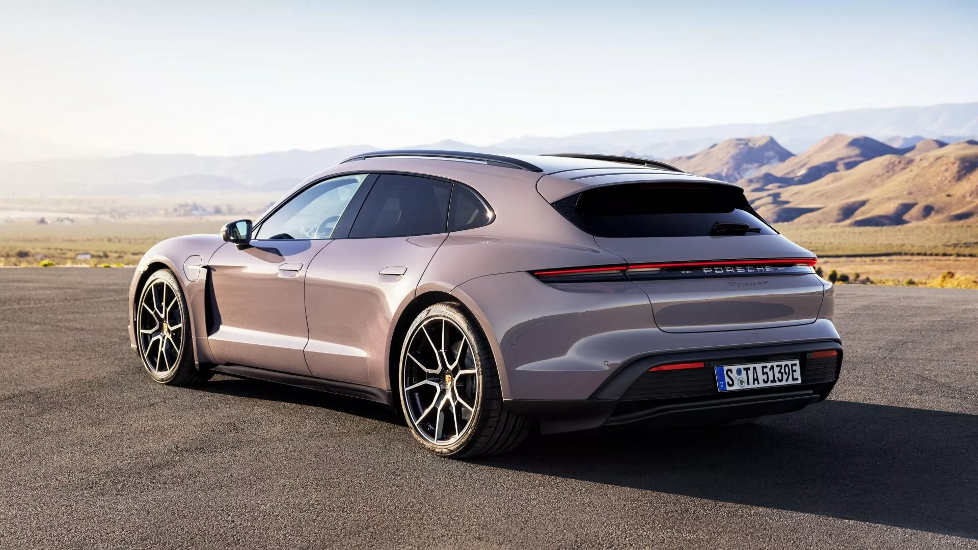 Vue arrière trois-quarts de la Porsche Taycan 2024 (Y1A Facelift) montrant son profil aérodynamique, toit panoramique, feux arrière horizontaux minces, diffuseur arrière, grandes roues en alliage à multiples branches, poignées de porte affleurantes et finition mate