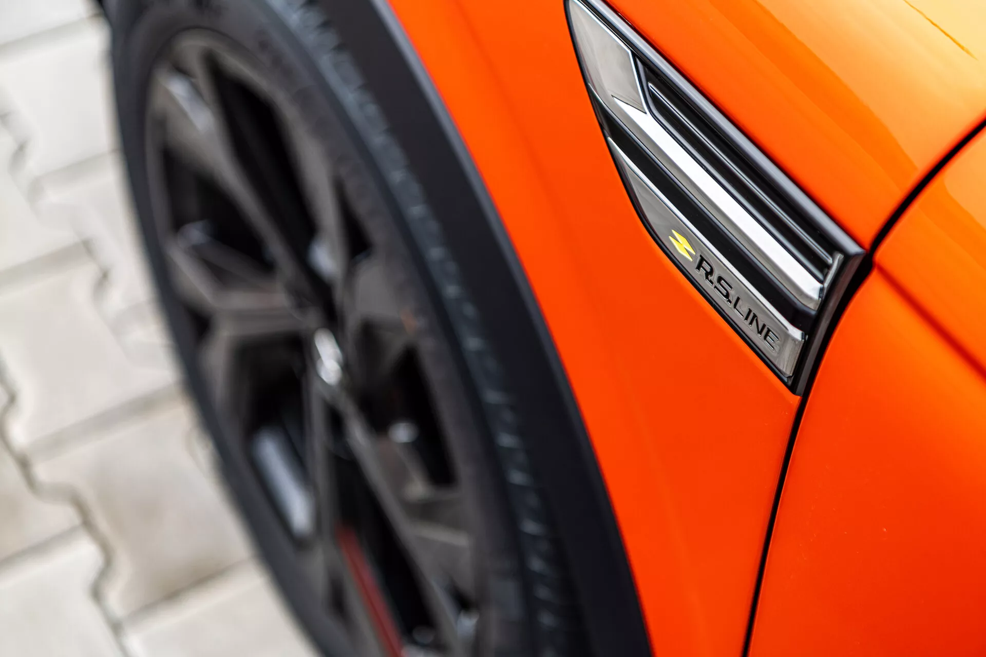Vue rapprochée d'une Renault Arkana orange de 2021 montrant le profil latéral avec un focus sur l'insigne S-Line, l'aile et le design sportif de la roue depuis un angle bas