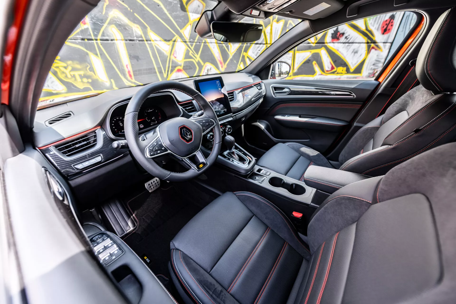 Vue intérieure de la Renault Arkana 2021 depuis le côté passager mettant en avant le volant avec commandes médias et régulateur de vitesse, tableau de bord numérique, système d’infodivertissement, boîte de vitesses automatique, sièges sportifs avec finitions de luxe et fonctionnalités technologiques avancées