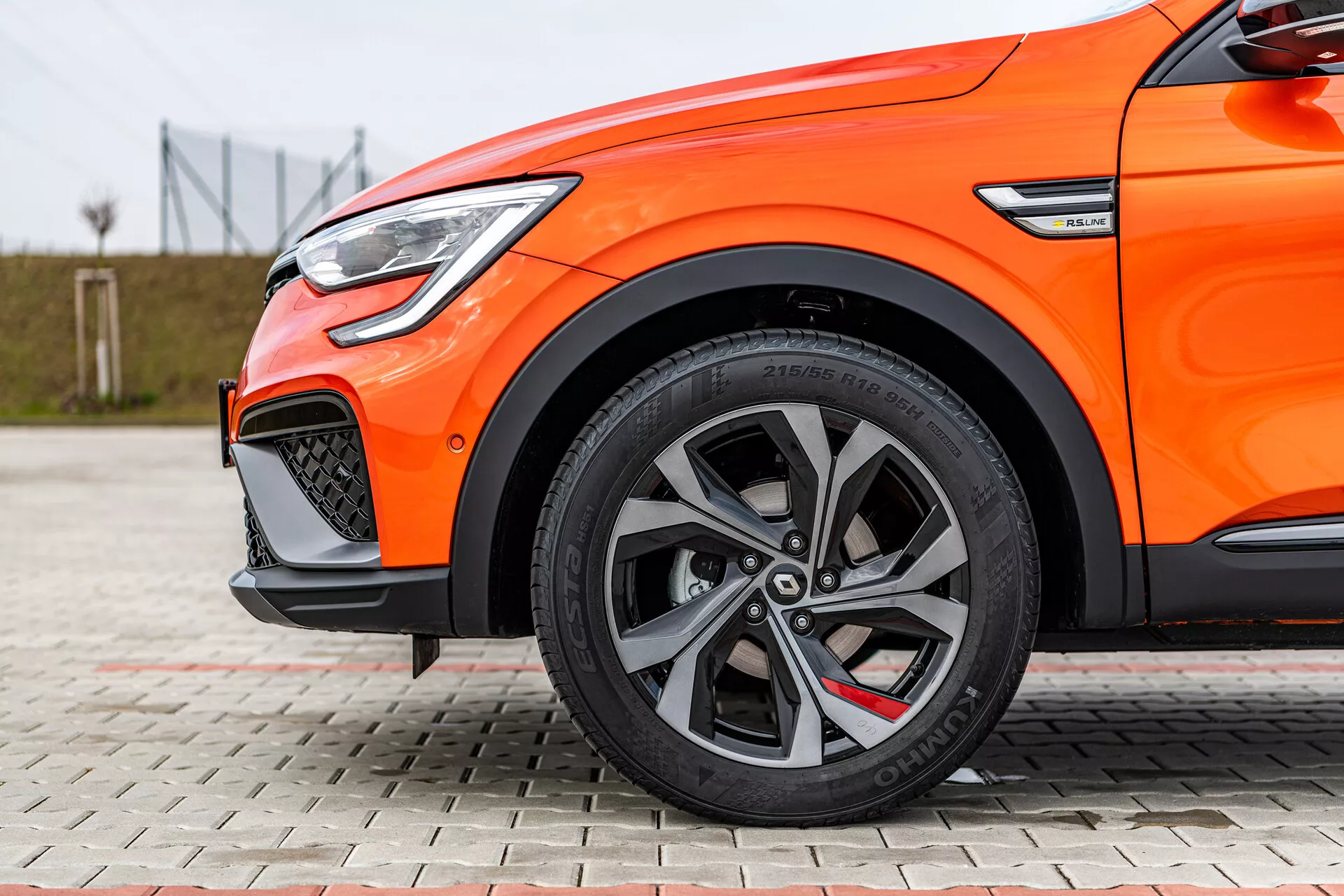 Vue latérale rapprochée d'une Renault Arkana 2021 orange mettant en évidence des roues en alliage à multiples branches, des pneus à profil bas, un système de freinage haute performance et des feux diurnes LED