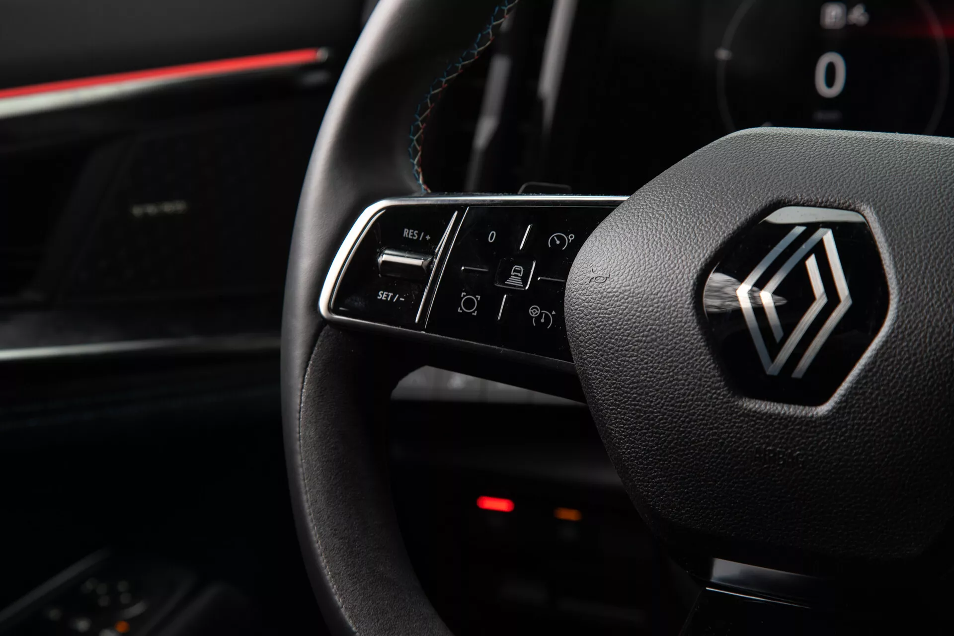 Vue intérieure du Renault Austral 2022 mettant en évidence les commandes du volant et l'emblème, y compris les fonctions de boutons illuminés pour le volume, les appels, les commandes vocales et la navigation infotainment, du point de vue du siège du conducteur.