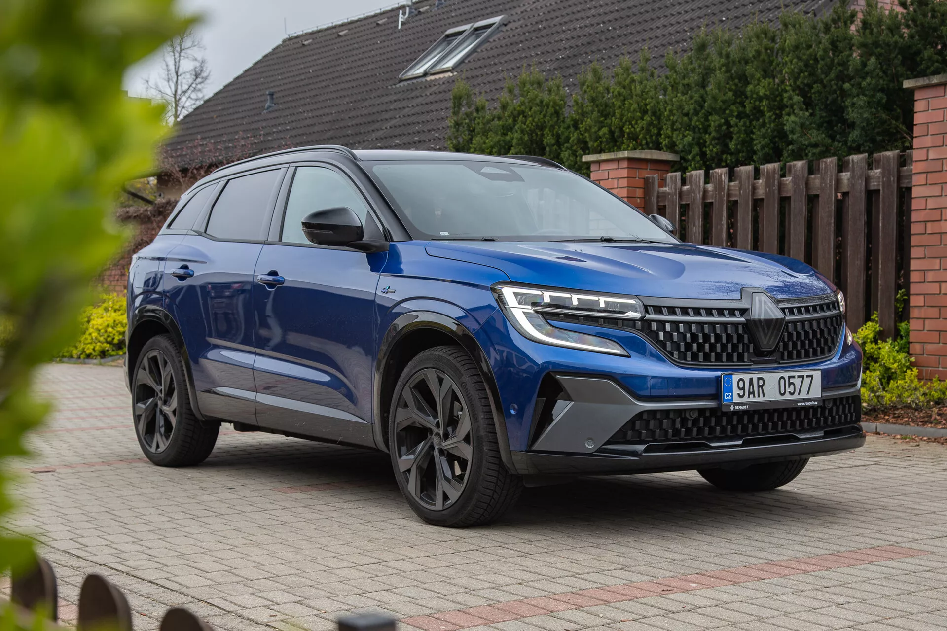SUV moderne Renault Austral 2022 présenté sous un angle avant trois quarts mettant en avant des phares LED, une grille proéminente, des roues en alliage élégantes et une carrosserie dynamique avec finition peinture métallisée, photographié sous un angle bas pour souligner sa stature et ses caractéristiques de design sur un fond résidentiel.