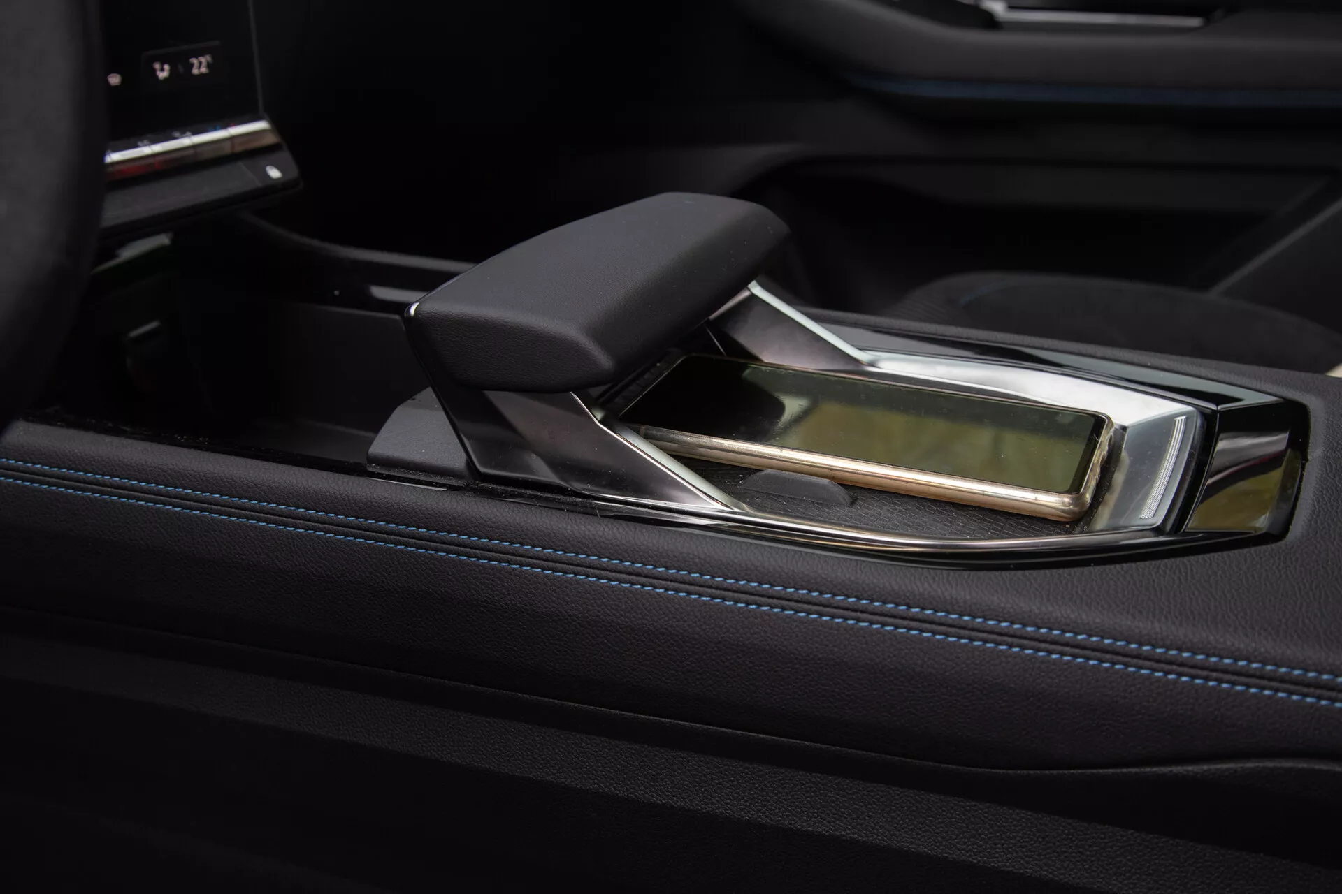 Vue rapprochée de la console centrale luxueuse du Renault Austral 2022 avec un levier de vitesse automatique moderne, présentant un design ergonomique avec des accents en cuir et chrome, sur un fond d'habillage noir brillant et une interface de commande d'infodivertissement sophistiquée.