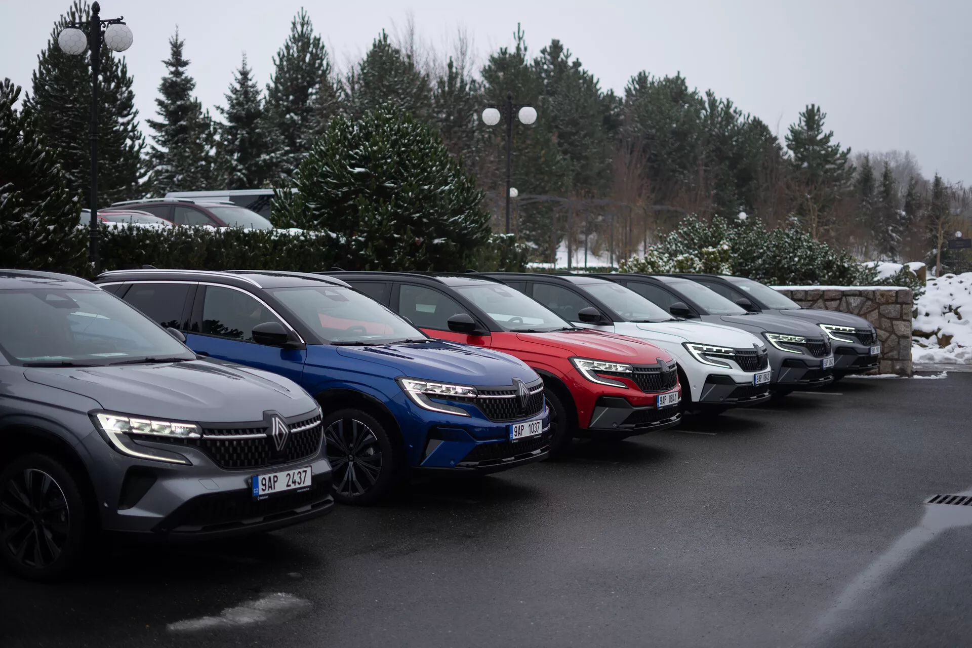 Alignement de cinq voitures Renault Austral 2022 garées à 45 degrés sur un parking hivernal, présentant des modèles en gris foncé, bleu, rouge, argent et gris, avec phares LED et grilles avant modernes