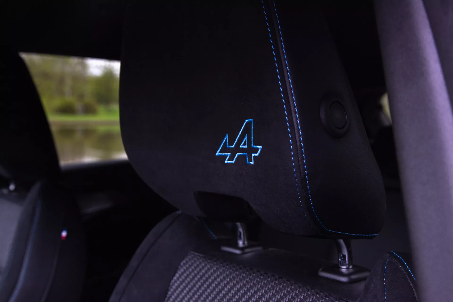 Vue rapprochée de l'intérieur de la Renault Austral 2022 montrant le siège du conducteur en tissu noir avec une couture bleue distinctive et un logo 'A' stylisé sur l'appuie-tête, guide de ceinture de sécurité intégré visible, suggérant des caractéristiques de véhicule moderne et possiblement sportif.