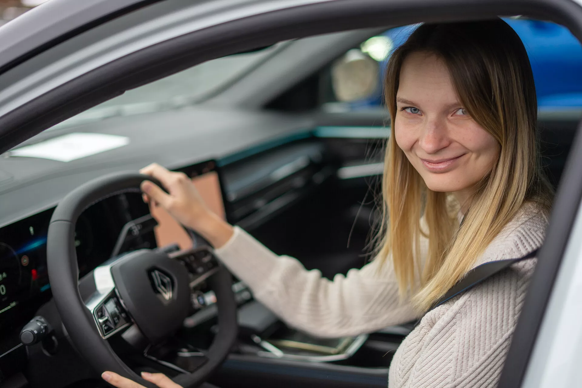 Vue intérieure du Renault Austral 2022 centrée sur le côté conducteur avec une femme au siège conducteur, mettant en vedette des commandes montées sur le volant, un tableau de bord numérique, et une console centrale avec interface tactile.
