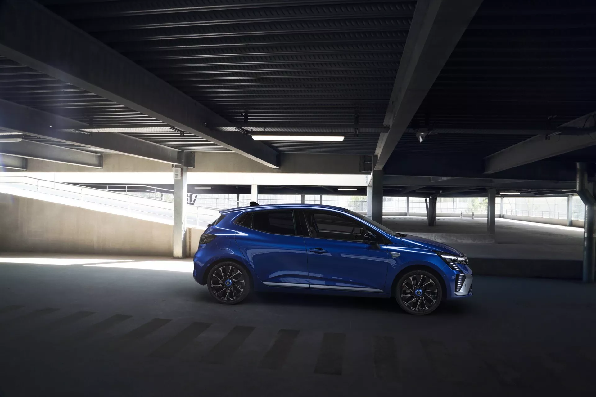 Hatchback bleu Renault Clio V-facelift 2023 garée en angle dans un parking sombre, mettant en évidence son design élégant, ses jantes en alliage et ses fonctionnalités technologiques intégrées