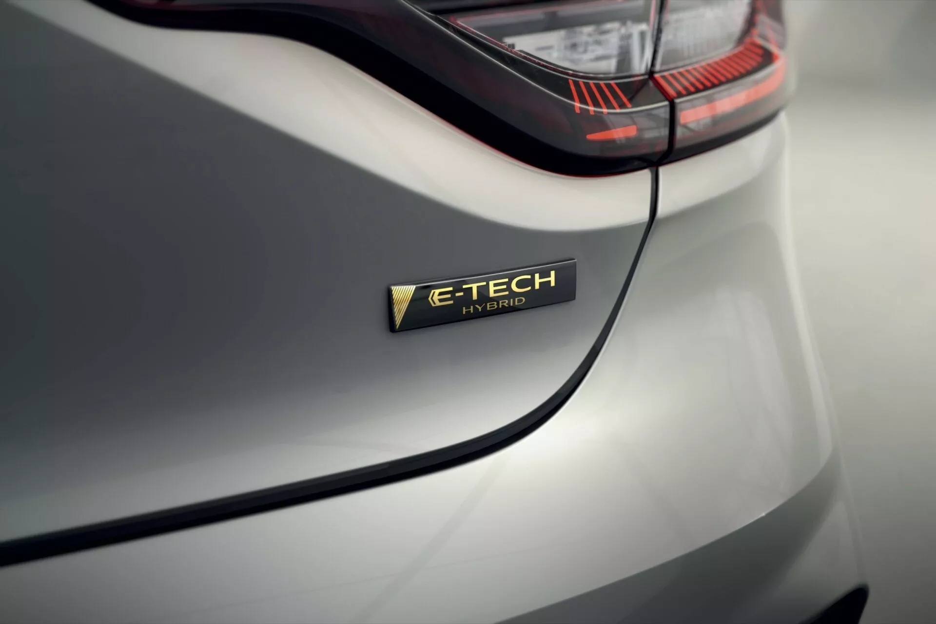 Vue rapprochée du badge E-TECH Hybrid sur la Renault Clio V-Facelift 2023, montrant la technologie hybride du véhicule et le design élégant de la carrosserie en gris clair