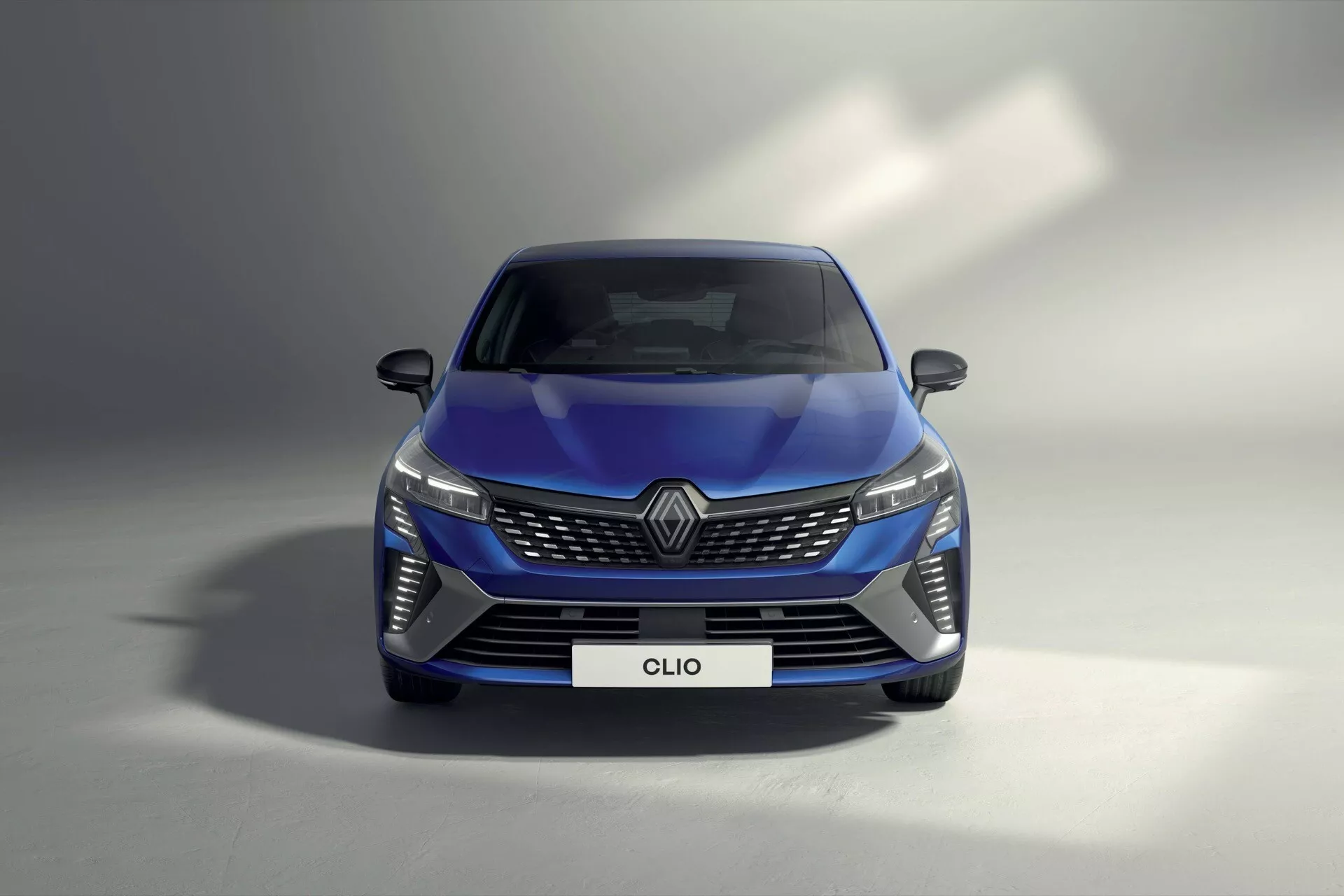 Renault Clio V Facelift 2023 en bleu présentant des phares LED, un design de grille complexe, un pare-chocs avant aérodynamique et des rétroviseurs de sécurité avancés depuis un angle avant bas soulignant la technologie d'éclairage automobile, les éléments de branding et le style aérodynamique.
