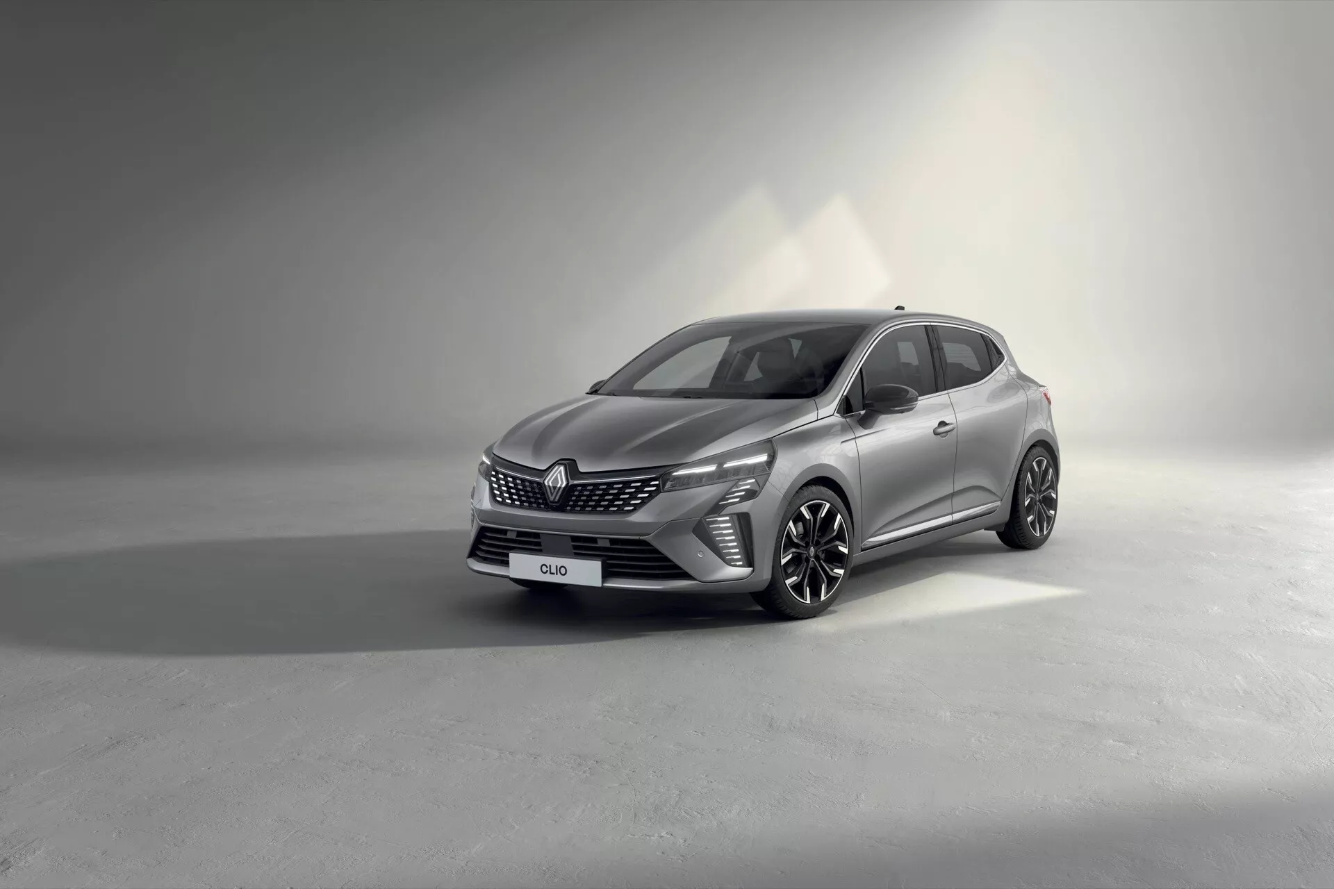 Modèle Renault Clio V-facelift 2023 présenté dans un cadre de studio, mettant en avant son design moderne et ses caractéristiques depuis une perspective frontale de trois quarts, soulignant la grille du véhicule, les phares LED, les roues en alliage à multiples branches et la carrosserie sophistiquée avec un éclairage contrôlé pour accentuer les détails.