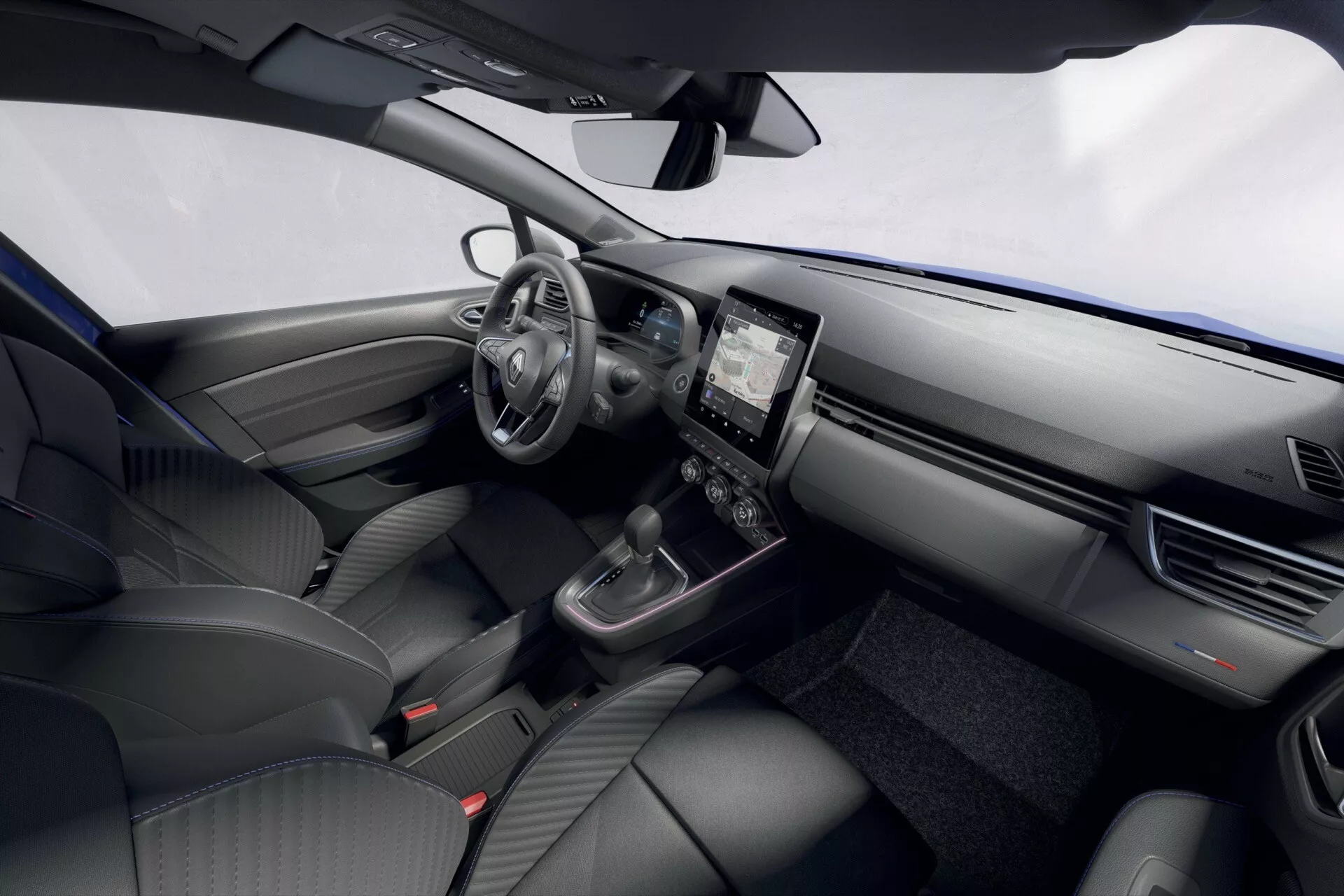 Intérieur du Renault Clio facelift 2023 montrant le tableau de bord, le volant avec des commandes montées, le cluster d’instruments numérique, le système d’infotainment tactile, le contrôle du climat, le sélecteur de vitesse et les sièges avant depuis un angle élevé côté conducteur.