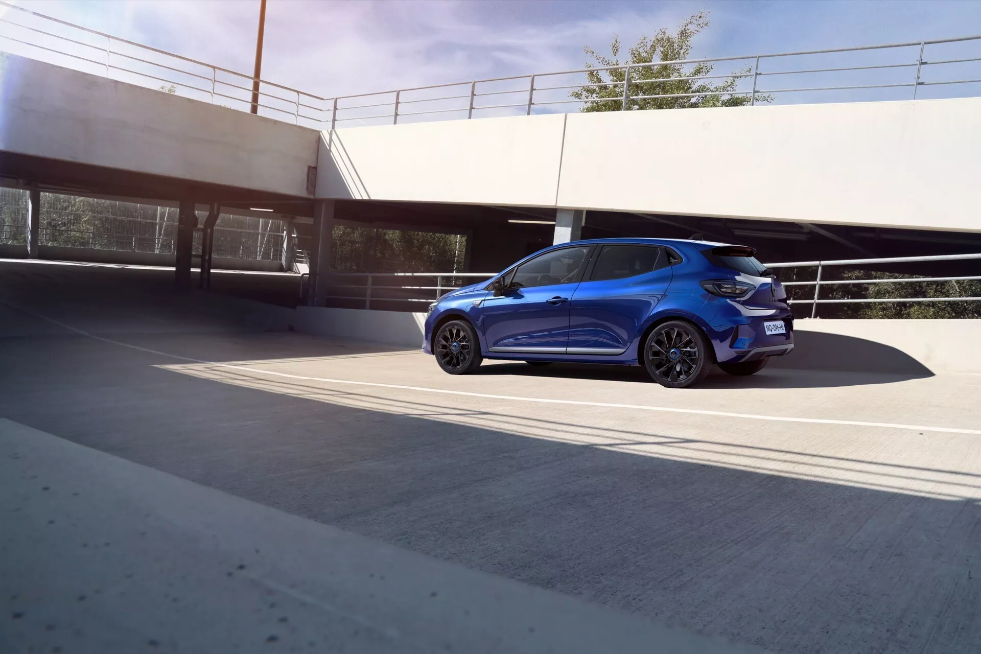 Renault Clio V-Facelift 2023, bleu métallisé, présentant des caractéristiques modernes avec des lumières LED, des roues en alliage, des vitres teintées et un design aérodynamique depuis une perspective arrière trois quarts dans un cadre urbain
