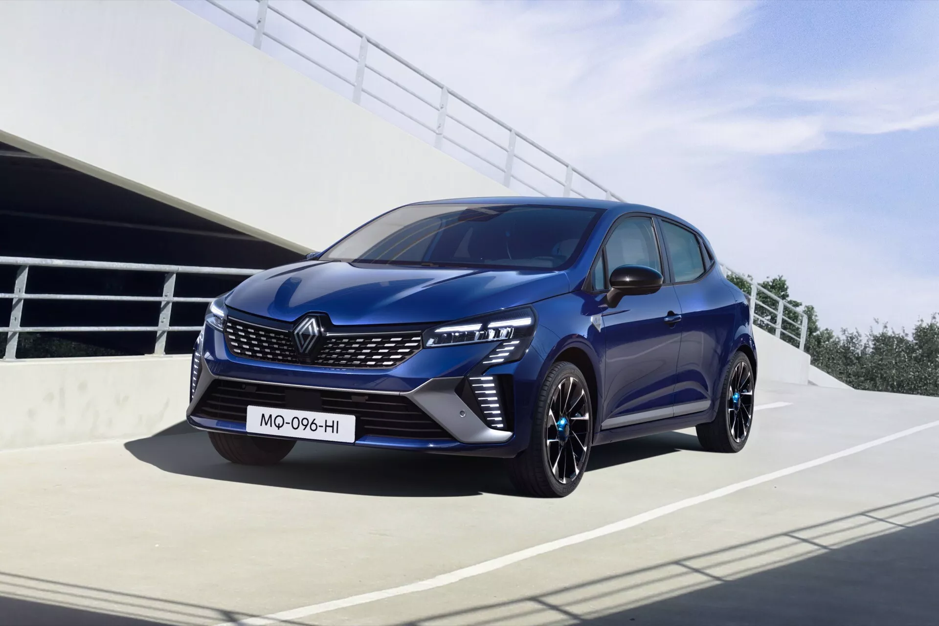 Hatchback moderne Renault Clio V Facelift 2023 en pose dynamique avec façade avant, phares LED, pare-chocs sportif avec entrées d'air, jantes en alliage et peinture bleu foncé, photographié dans un cadre urbain