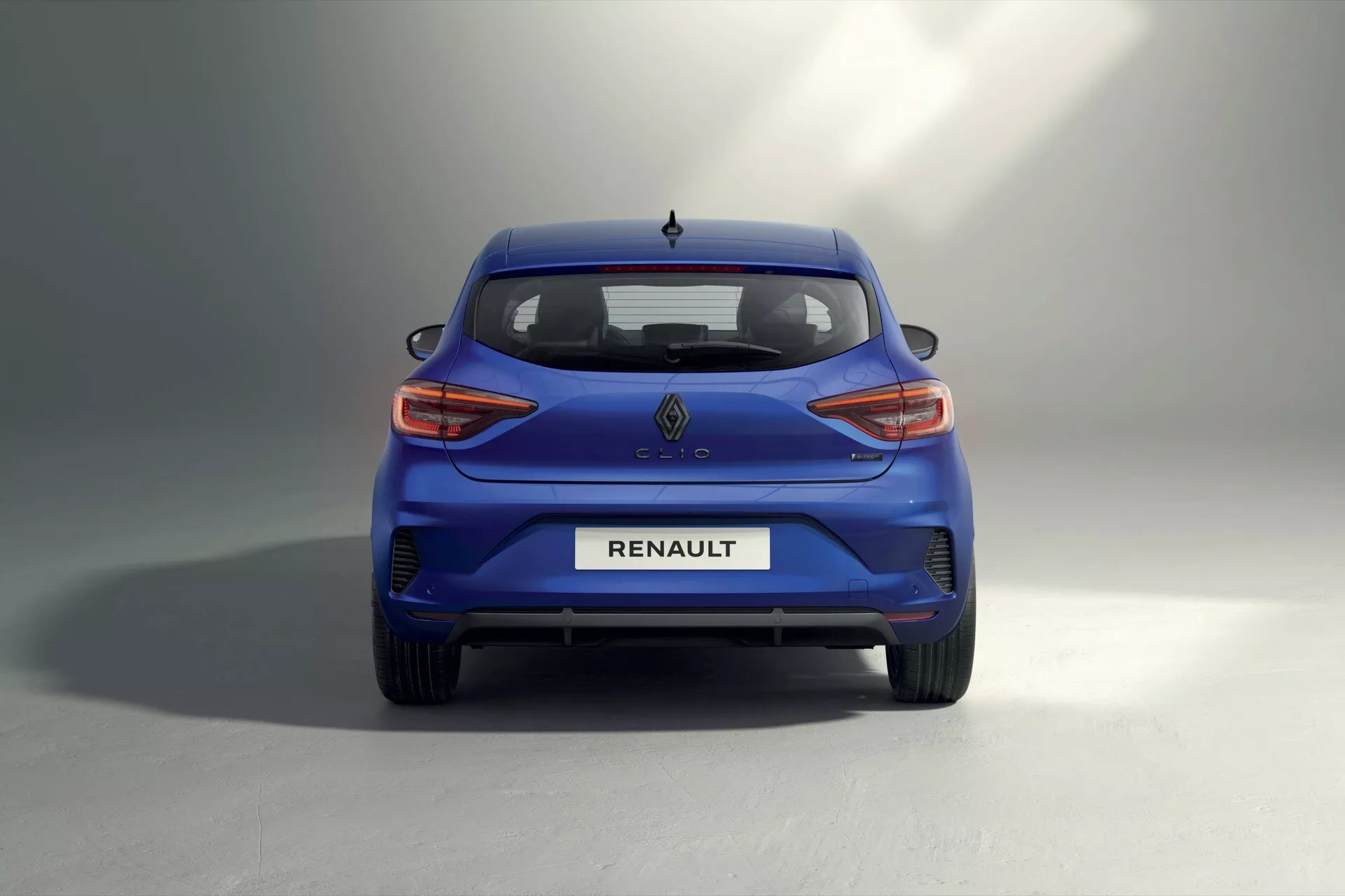 Vue arrière du Renault Clio V-facelift 2023 montrant le design moderne de la hatchback bleue et les feux arrière LED, dans un spacieux studio avec un fond dégradé gris-blanc.